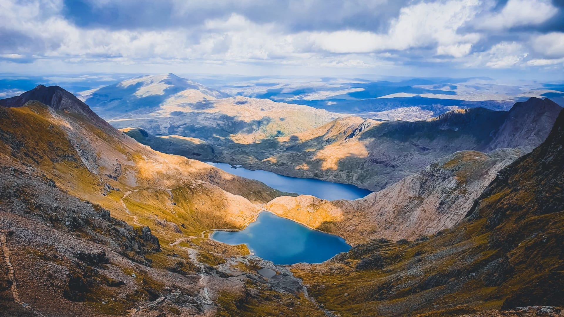 The jagged peak of Snowdon rising above a glacial lake in Snowdonia, low cloud catching on the ridgelines