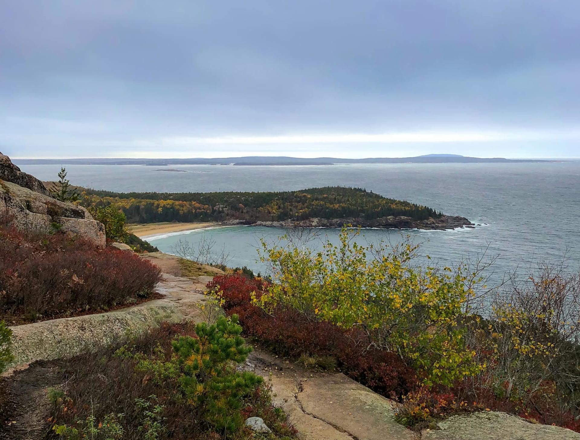 Pink and gold dawn light sweeping across the granite summit of Cadillac Mountain, with the island-dotted waters of Frenchman Bay glowing below.