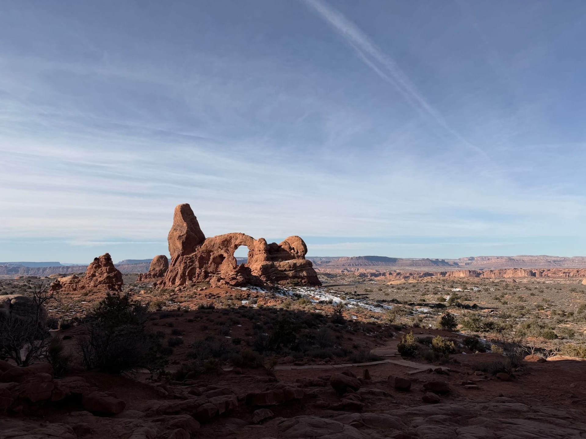 Delicate Arch glowing burnt orange at sunset against a deep blue Utah sky, framing the La Sal Mountains in the distance across a slickrock canyon