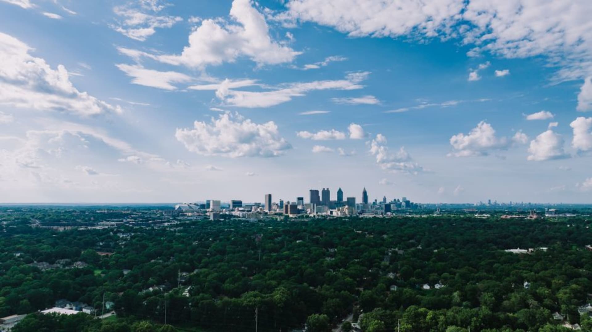Atlanta skyline rising above a canopy of green trees at dusk