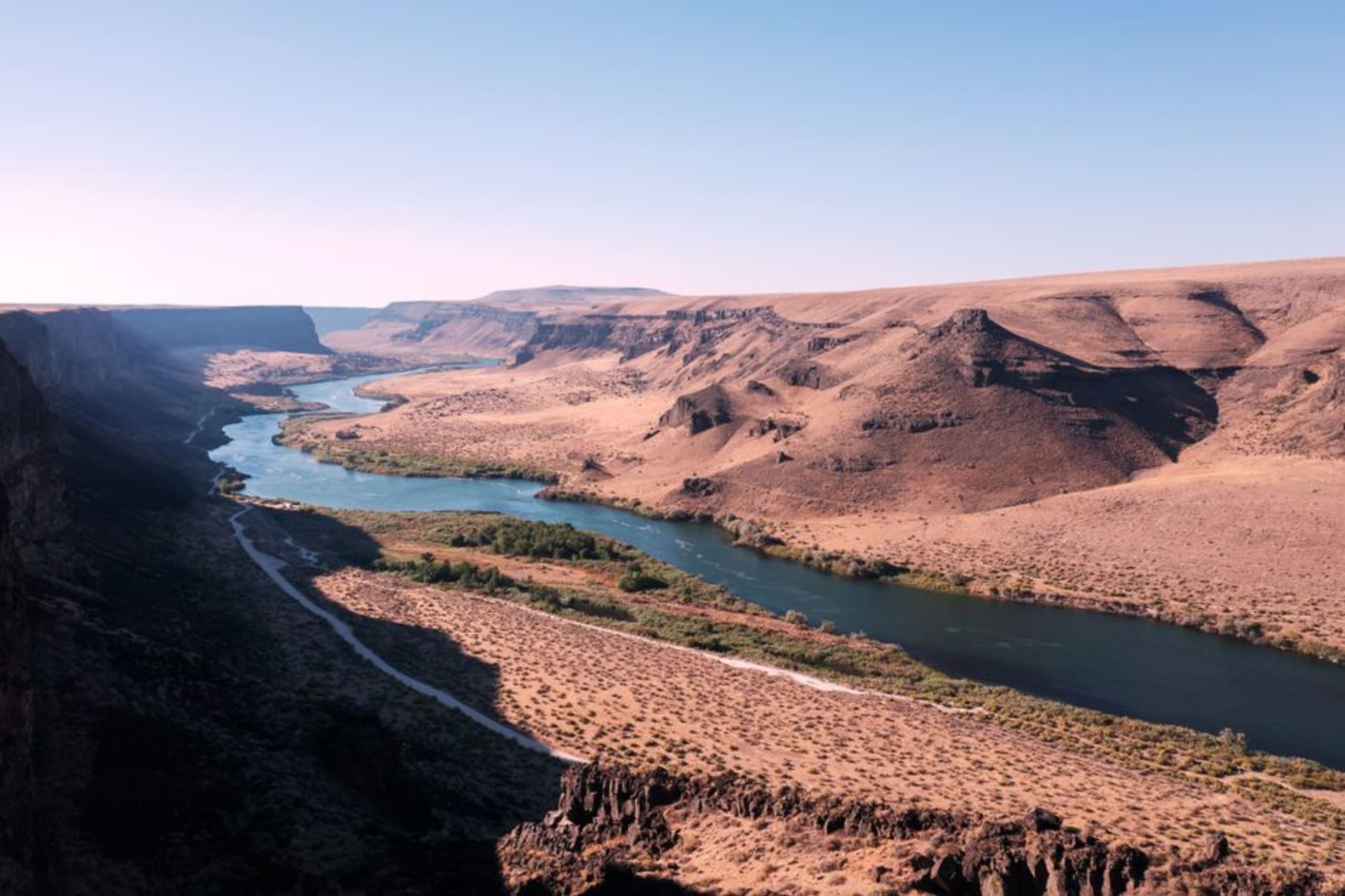 The Deschutes River winding through Bend, Oregon with pine forest and the snow-capped Cascade peaks in the distance