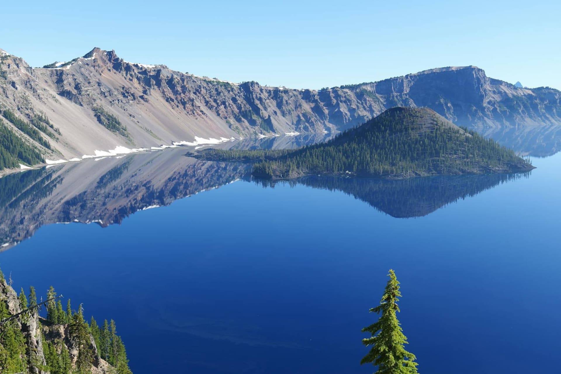 Aerial view of Crater Lake's impossibly deep blue water nestled inside the snow-dusted rim of a volcanic caldera, with Wizard Island rising from the center