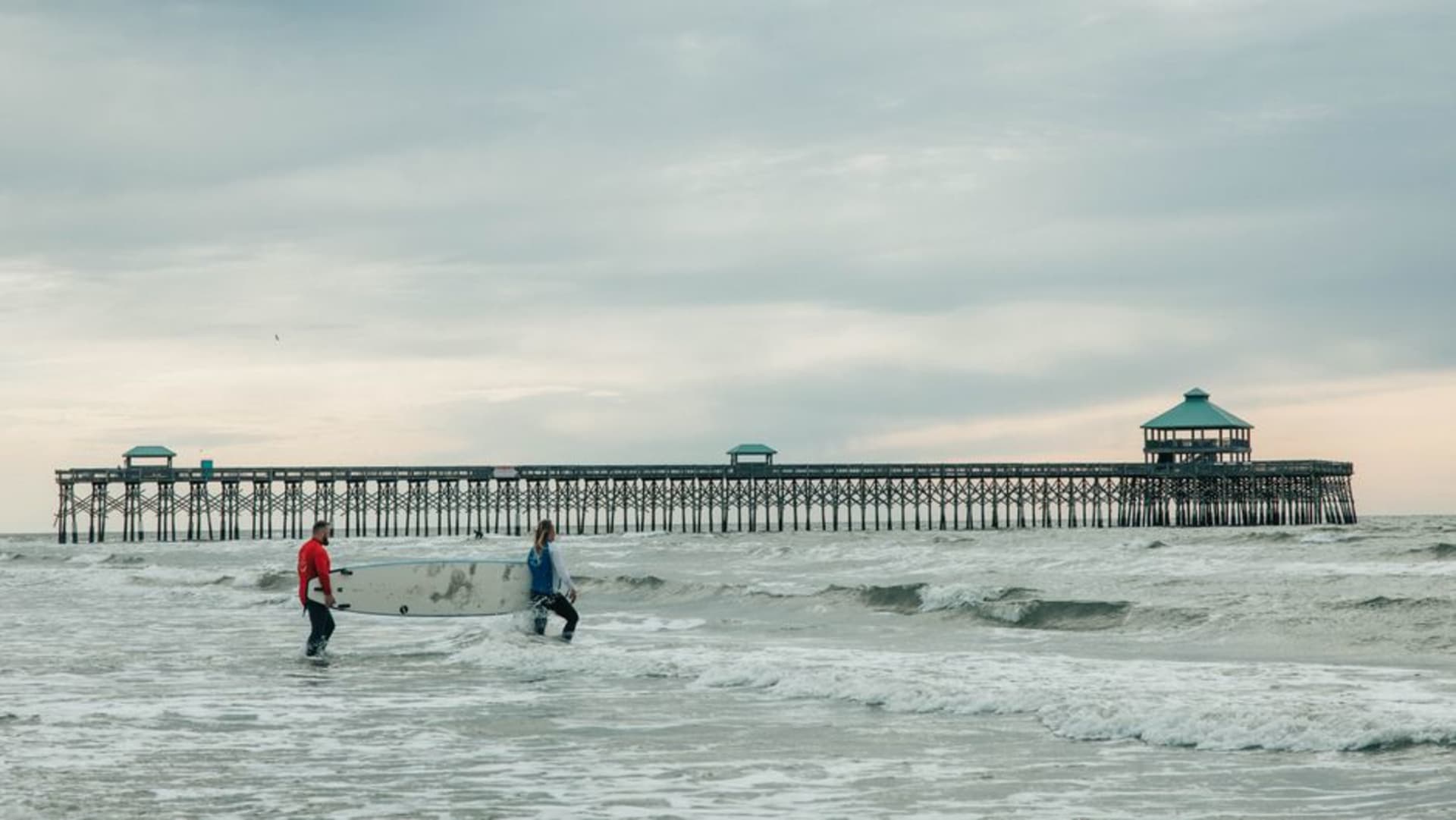Surfers in the water near the Folly Beach fishing pier in South Carolina at sunset