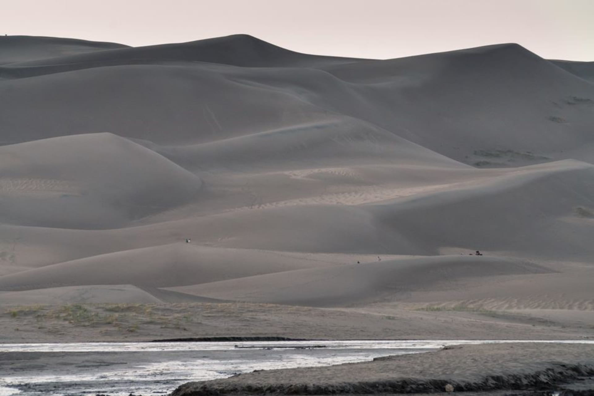 Towering sand dunes rising against snow-capped mountains under a blue sky