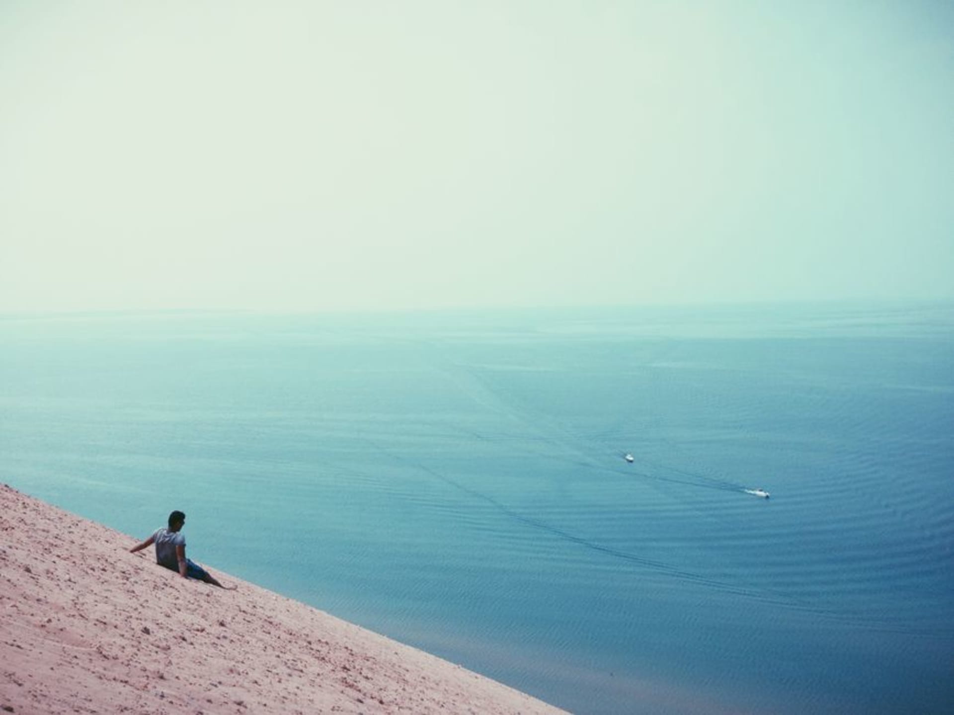 Sand dunes topped with marram grass sloping down to Lake Michigan under a pale sky