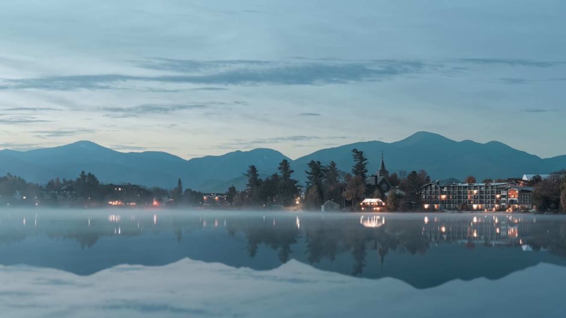 Mirror Lake reflecting forested Adirondack peaks at dawn in Lake Placid