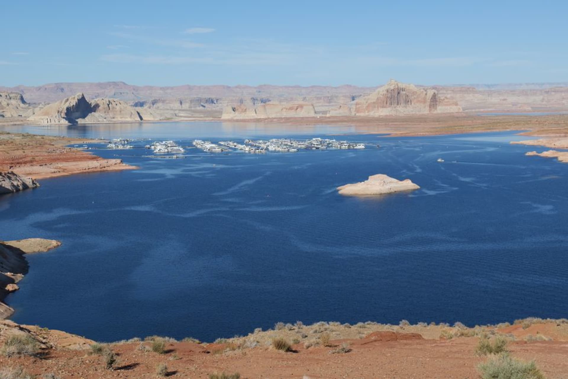 Turquoise water of Lake Powell winding between towering red and orange sandstone canyon walls under a wide desert sky