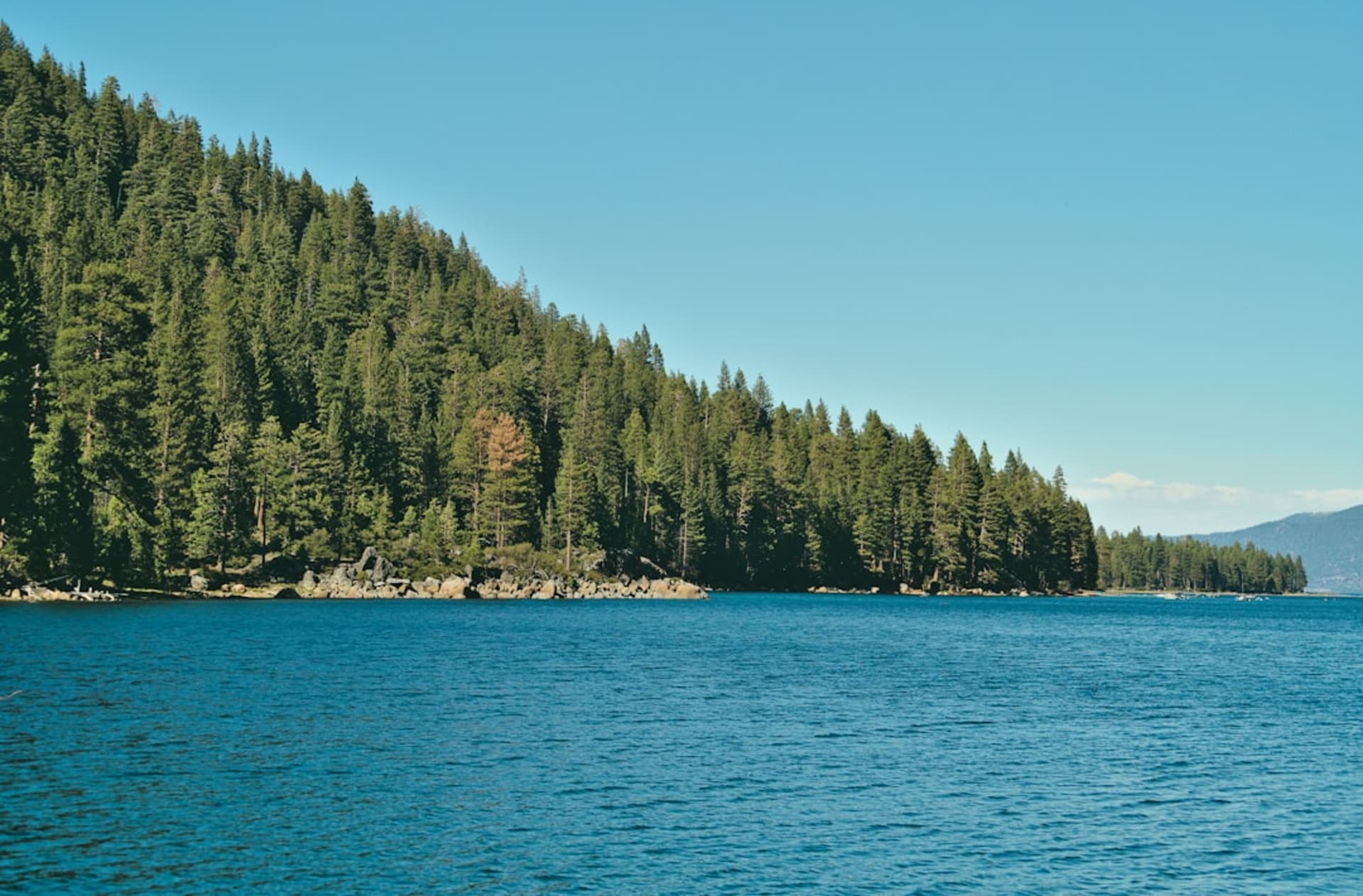 The deep blue expanse of Lake Tahoe seen from a granite overlook, ringed by pine forests and the snow-streaked peaks of the Sierra Nevada.