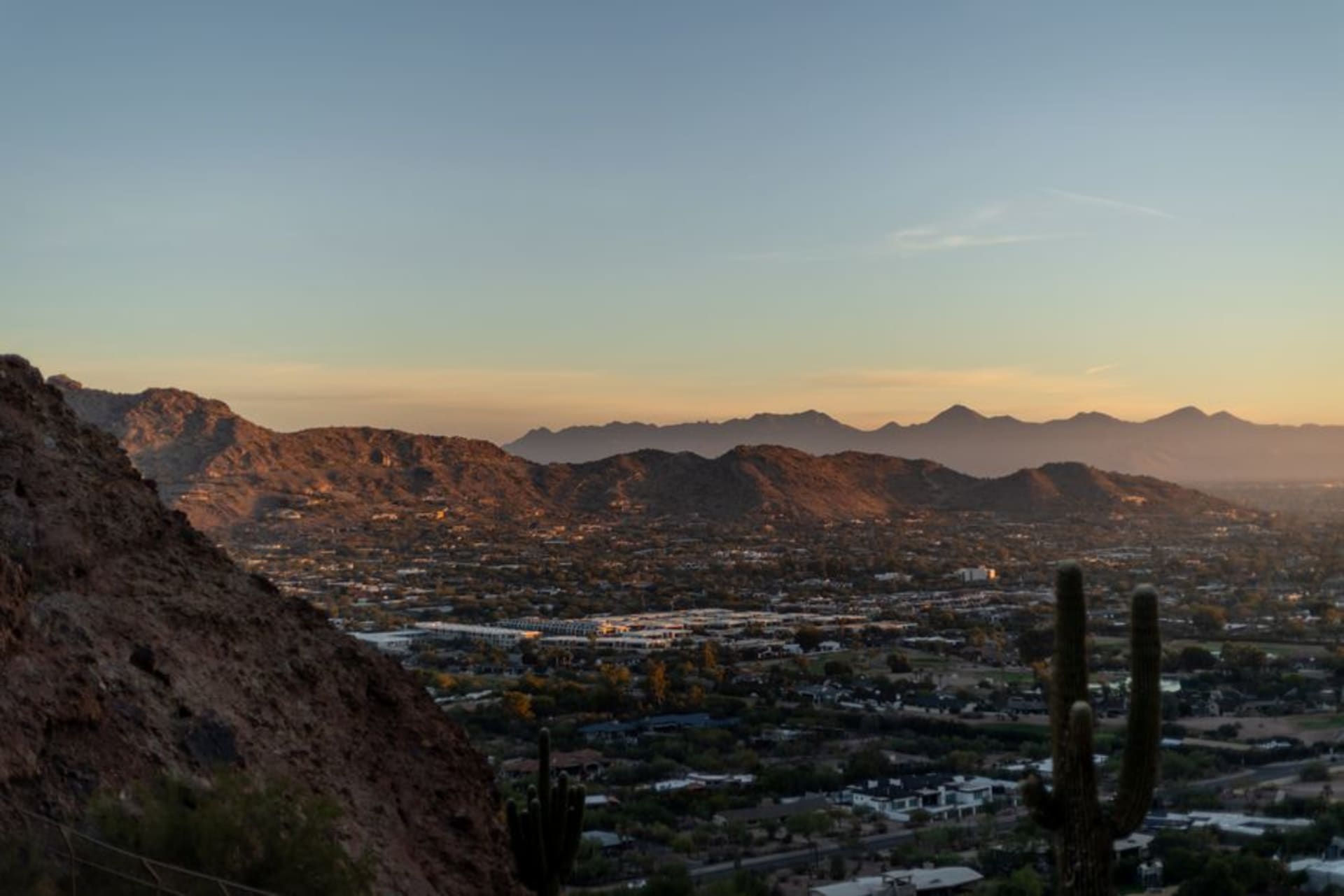 The Phoenix skyline at dusk with Camelback Mountain and saguaro-studded desert in the foreground under a burning orange sky