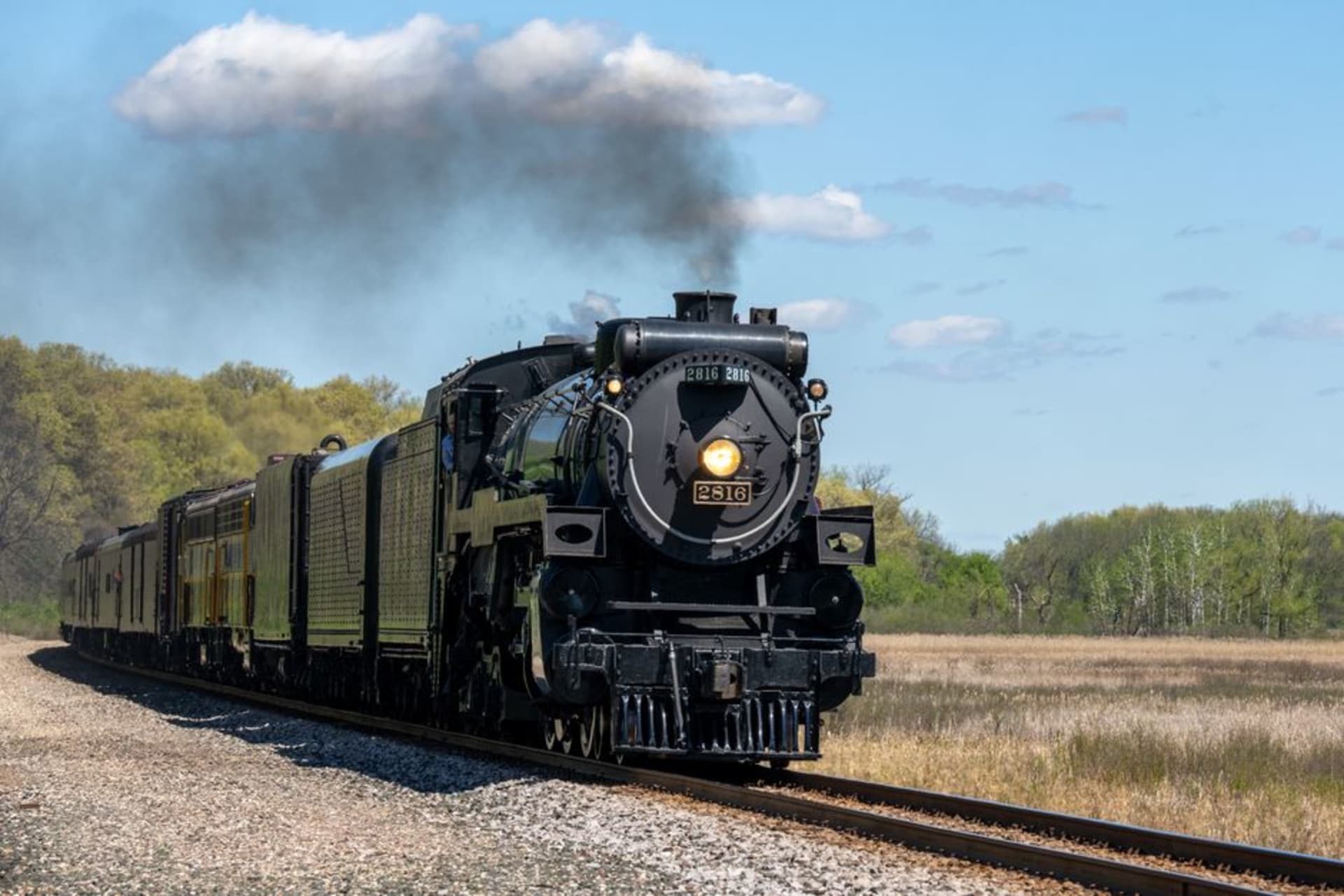 A vintage steam locomotive pulling passenger cars past farmland near Strasburg, Pennsylvania