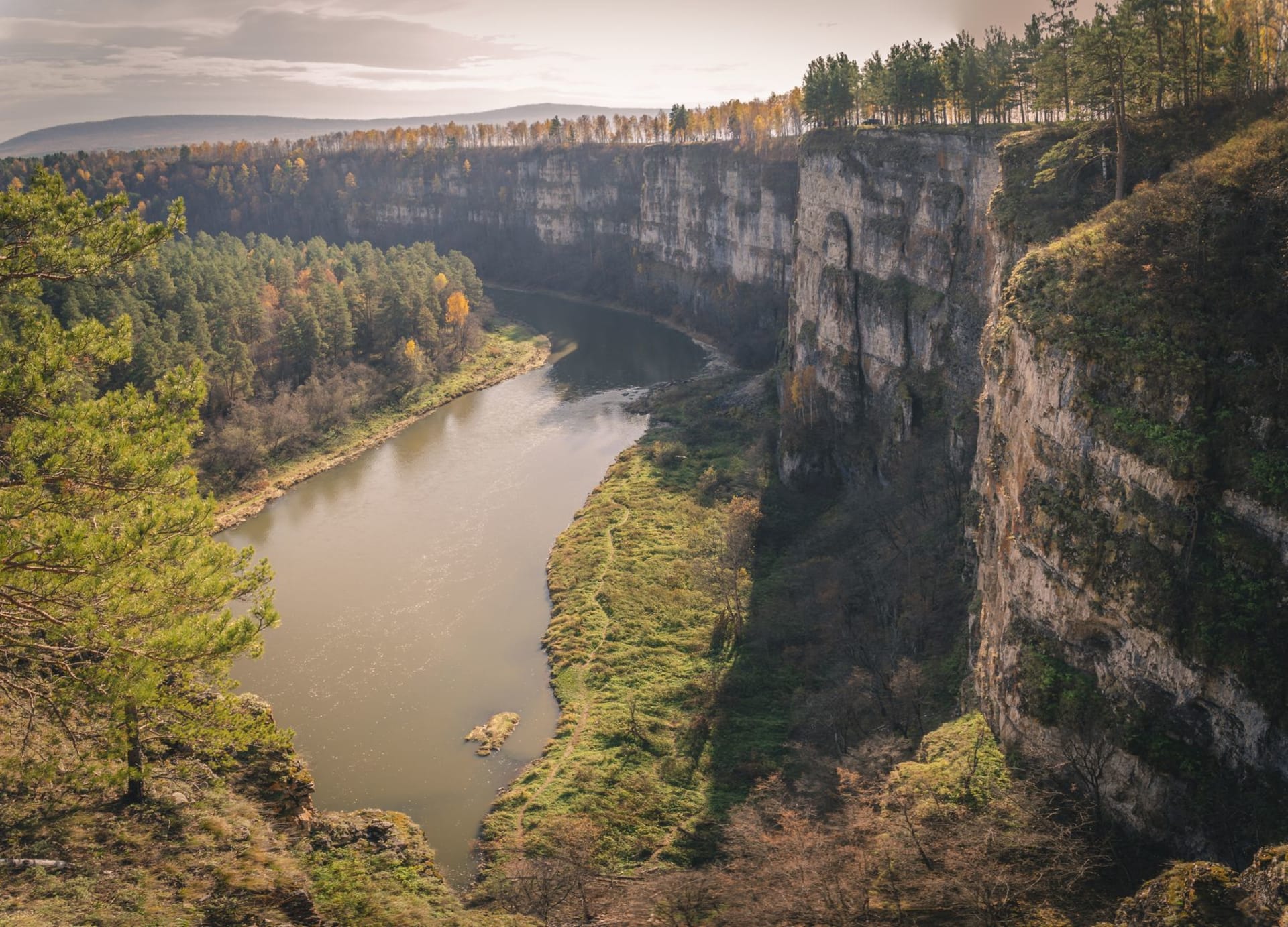 La rivière Inzer serpentant à travers un fond de vallée intact à l'aube, la brume s'élevant de l'eau, de sombres crêtes d'épicéas des deux côtés se reflétant dans la surface immobile près de la berge