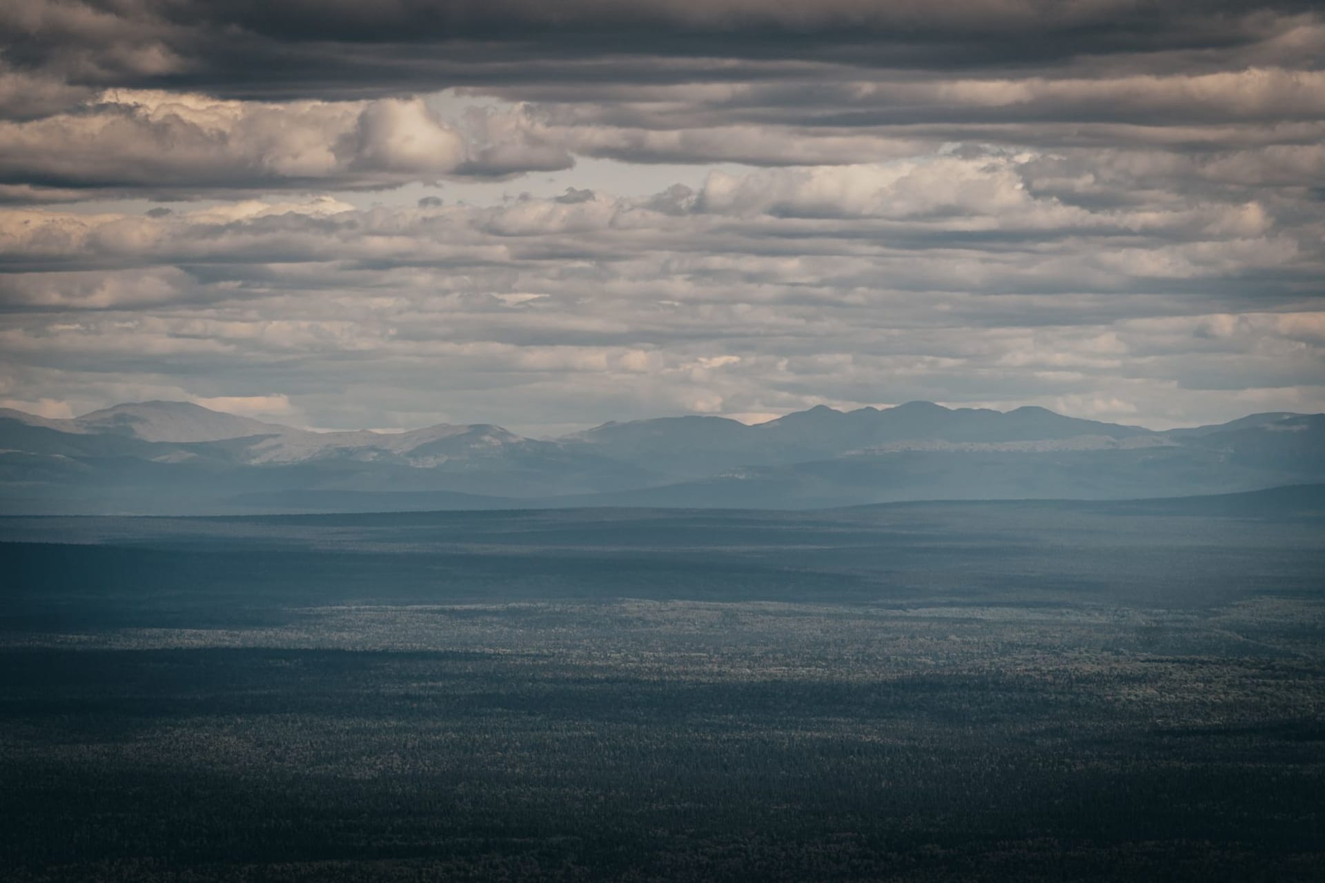 Rolling forested Ural mountain ridges under a wide open sky, endless taiga stretching to the horizon