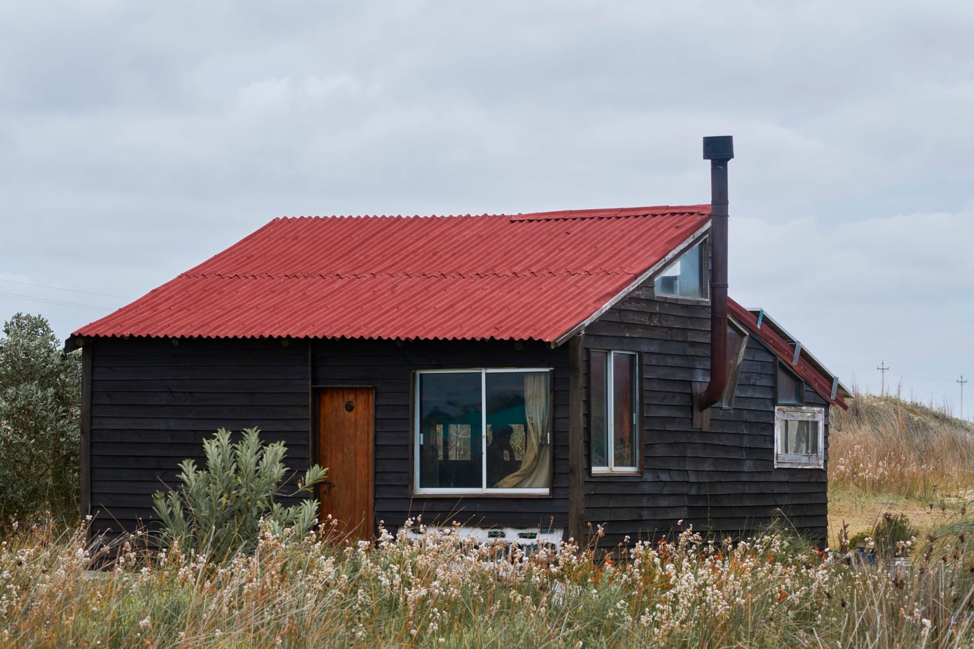 A lone lighthouse rising above sand dunes and a scattering of wooden shacks at the edge of a grey Atlantic sea