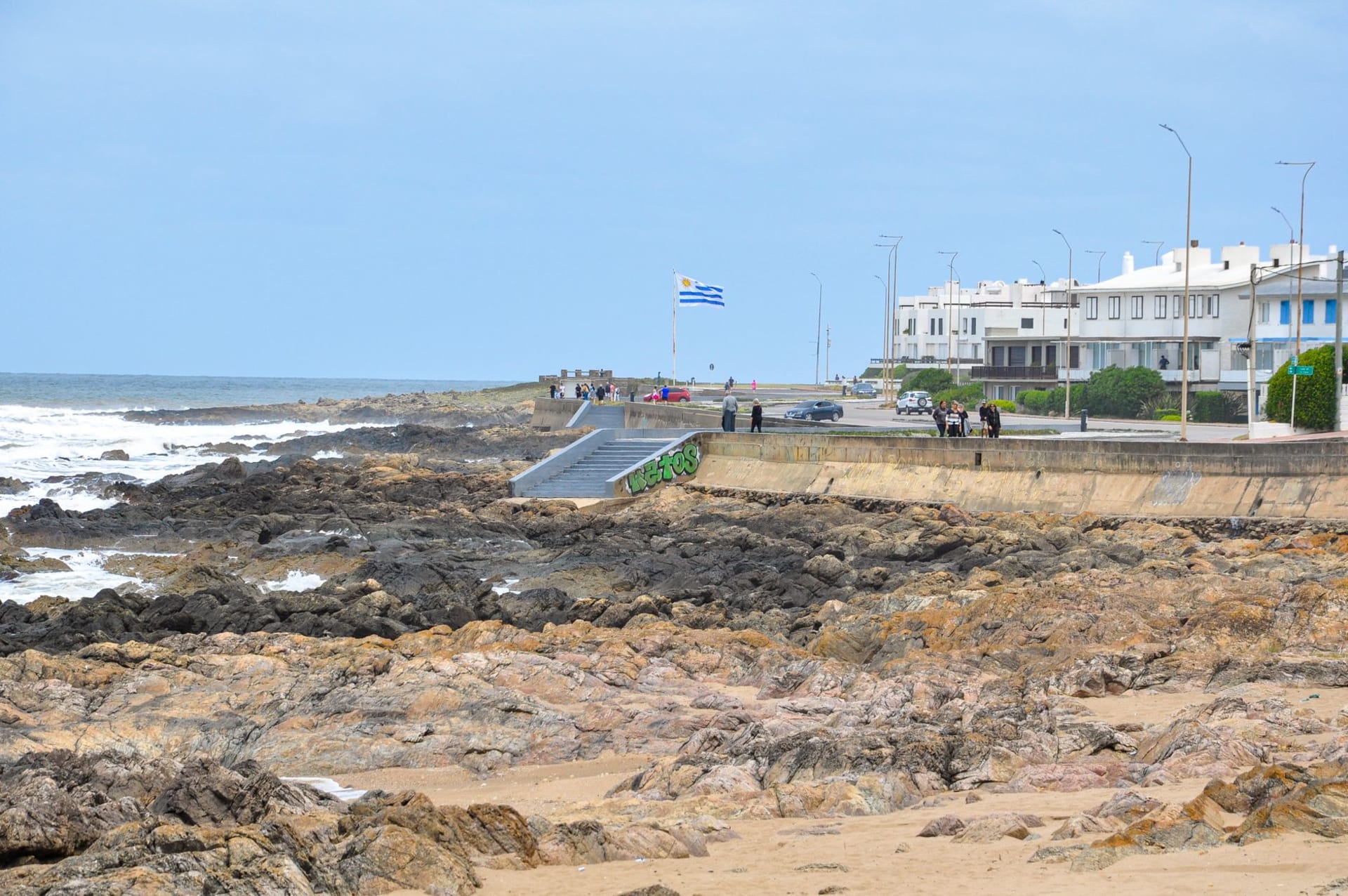 A red-capped white lighthouse on a rocky point above a surging Atlantic shore, with green coastal scrub and dark storm clouds building offshore