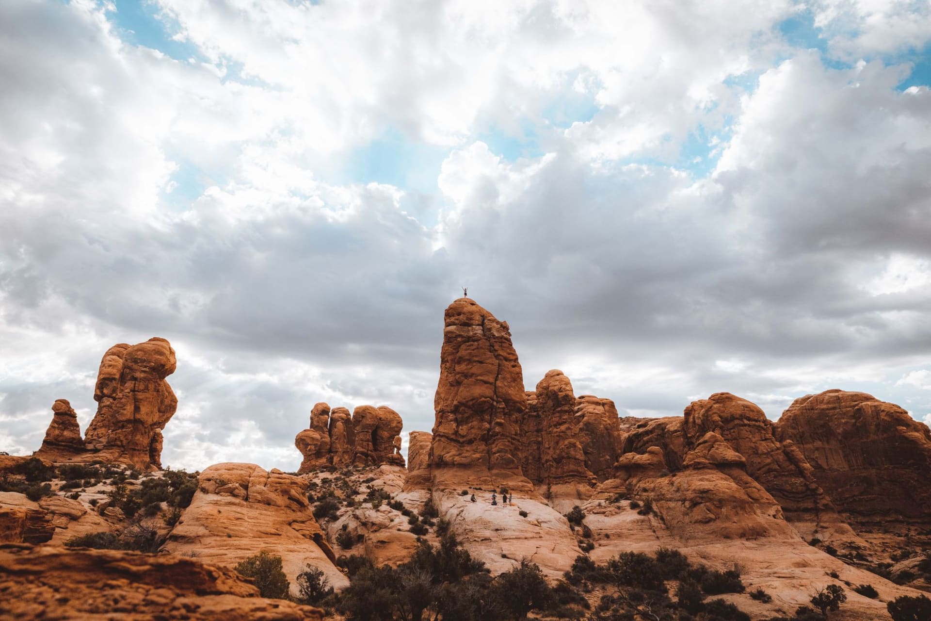 Delicate Arch standing alone on a sandstone bowl at sunset, framing the La Sal Mountains capped with snow in the distance