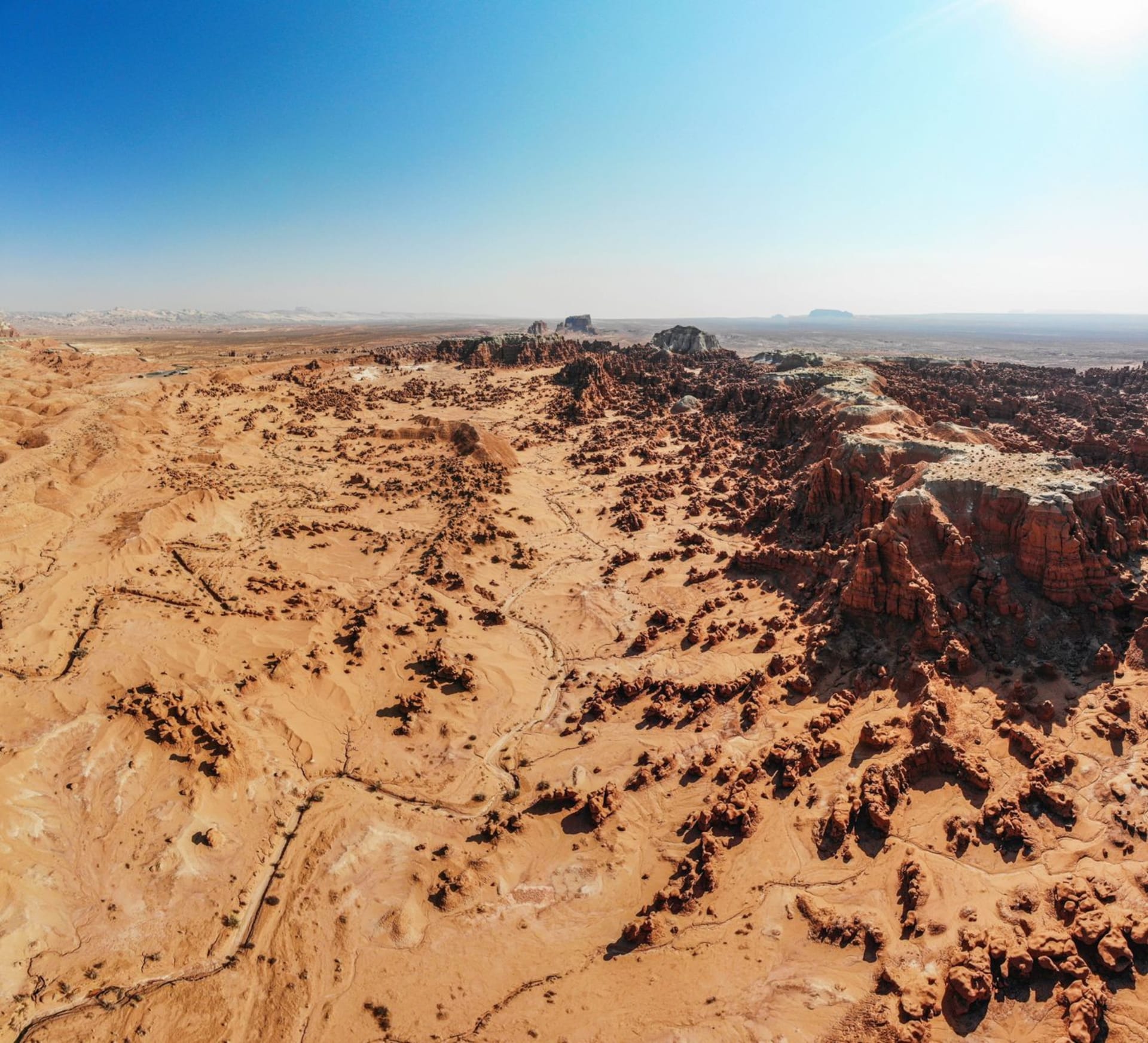 Hundreds of rounded orange sandstone goblin formations stretching across a valley floor under a cloudless sky, with mesas rising at the edges