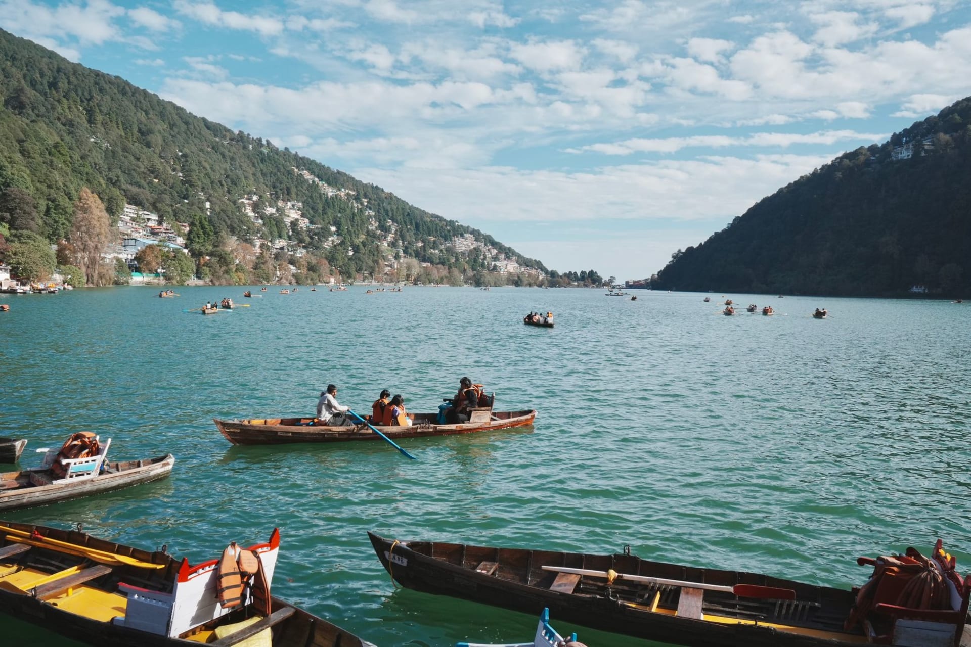 Naini Lake at dawn, rowing boats moored on still green water, the Naina Devi temple reflected in the far bank