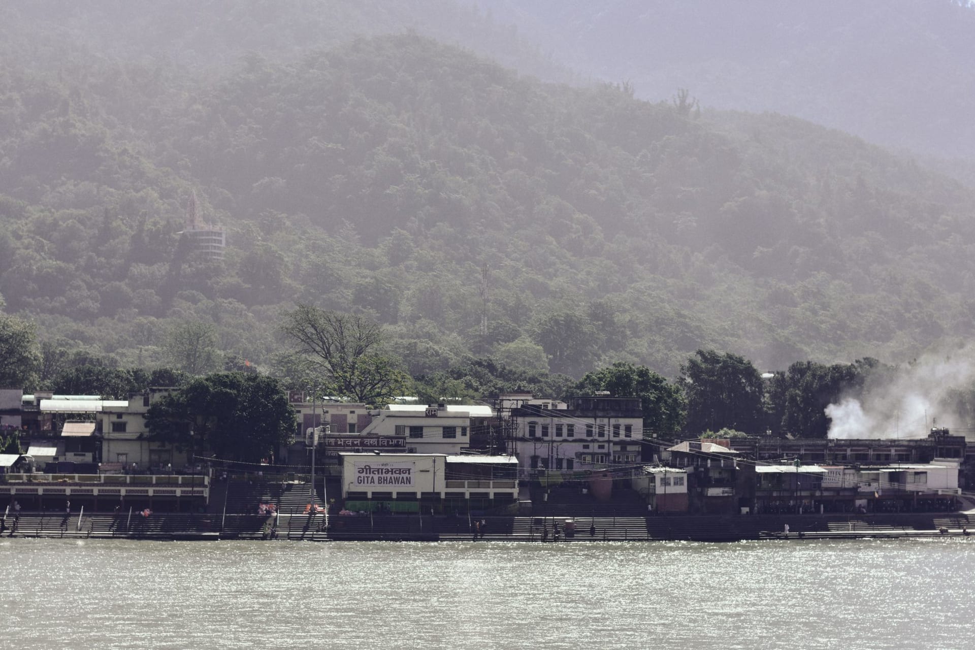 Laxman Jhula suspension bridge over the green Ganges at dusk, oil lamps floating downstream below