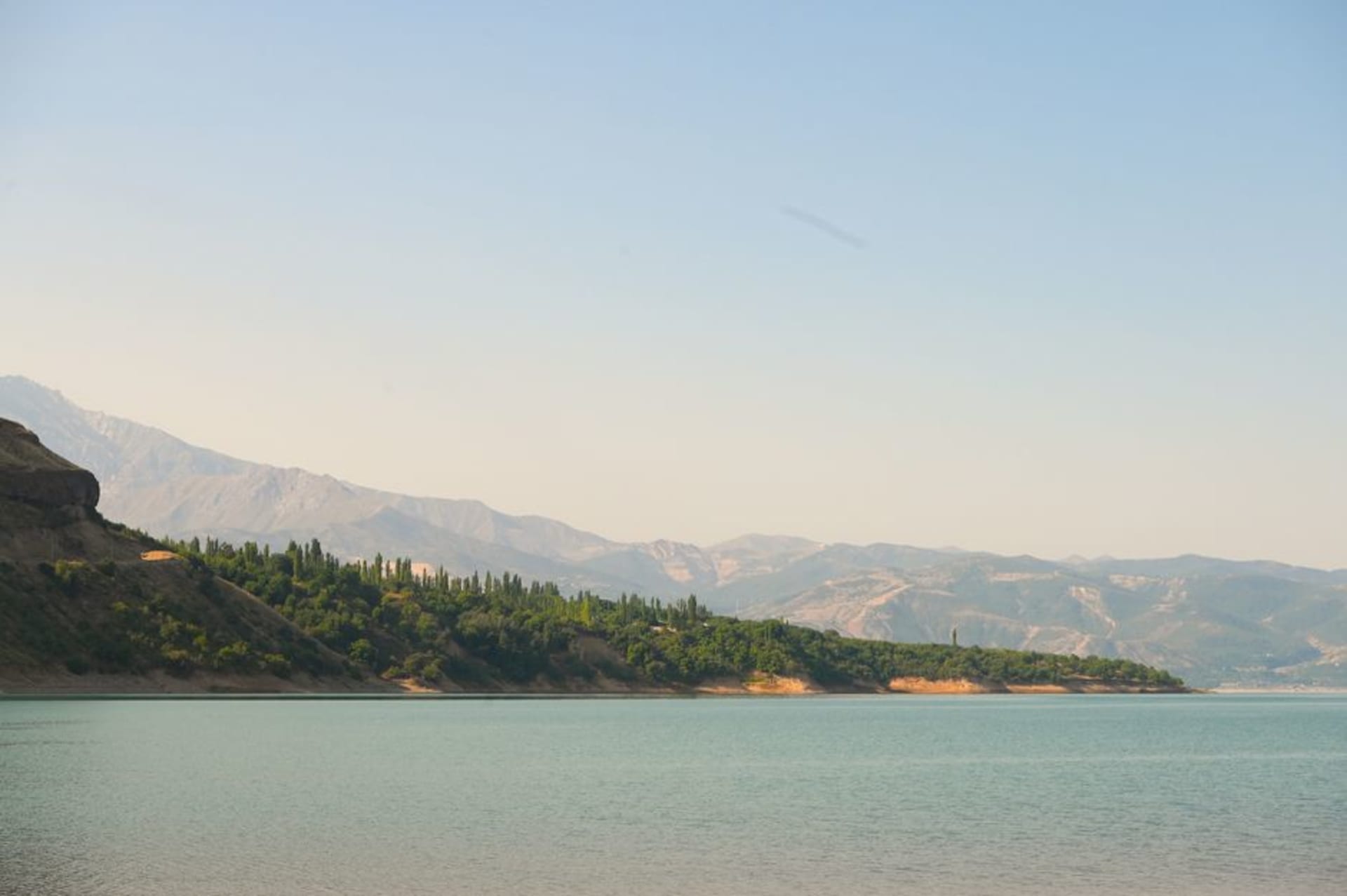 Turquoise reservoir waters surrounded by brown foothills with mountains in the distance