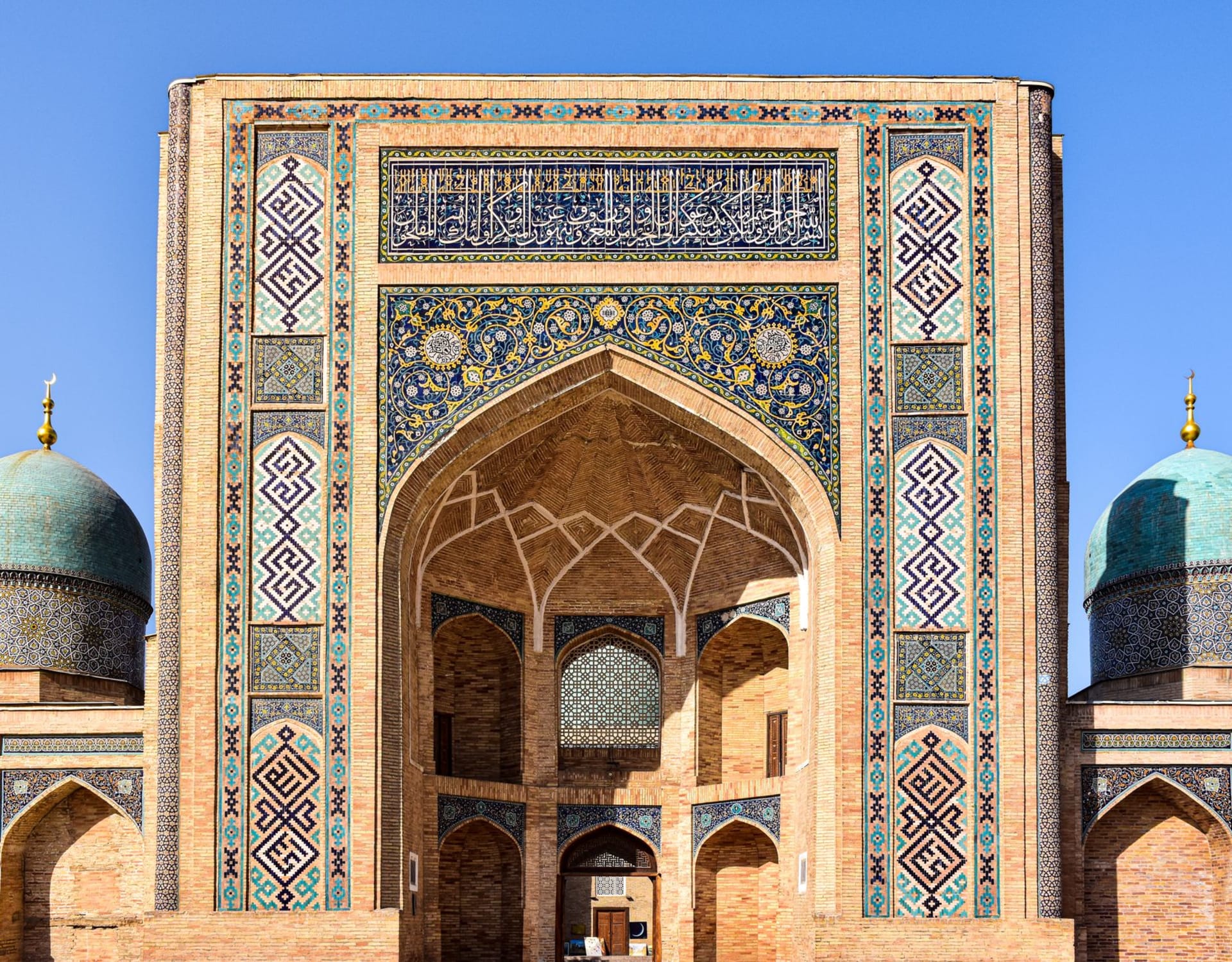 The colossal ruined portal of Ak-Saray Palace in Shakhrisabz, its twin turrets and tilework fragmentary against the Hissar Mountains, local families picnicking at its base