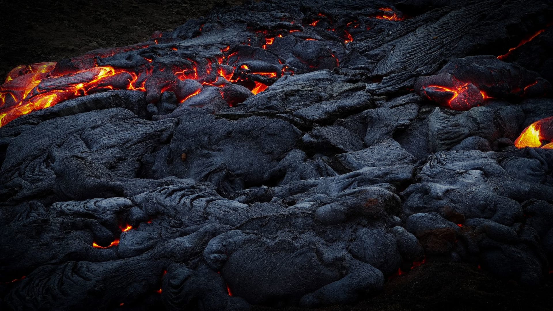 Twin volcanic peaks of Ambrym shrouded in sulfurous haze with black ash plains stretching toward a dark coastline