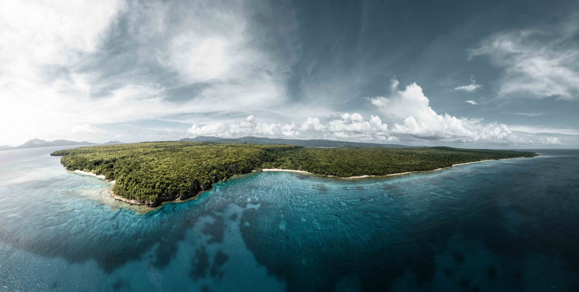 Gaua Island in the Banks group seen from the ocean with its forested volcanic slopes rising steeply from the sea under dramatic cloud cover