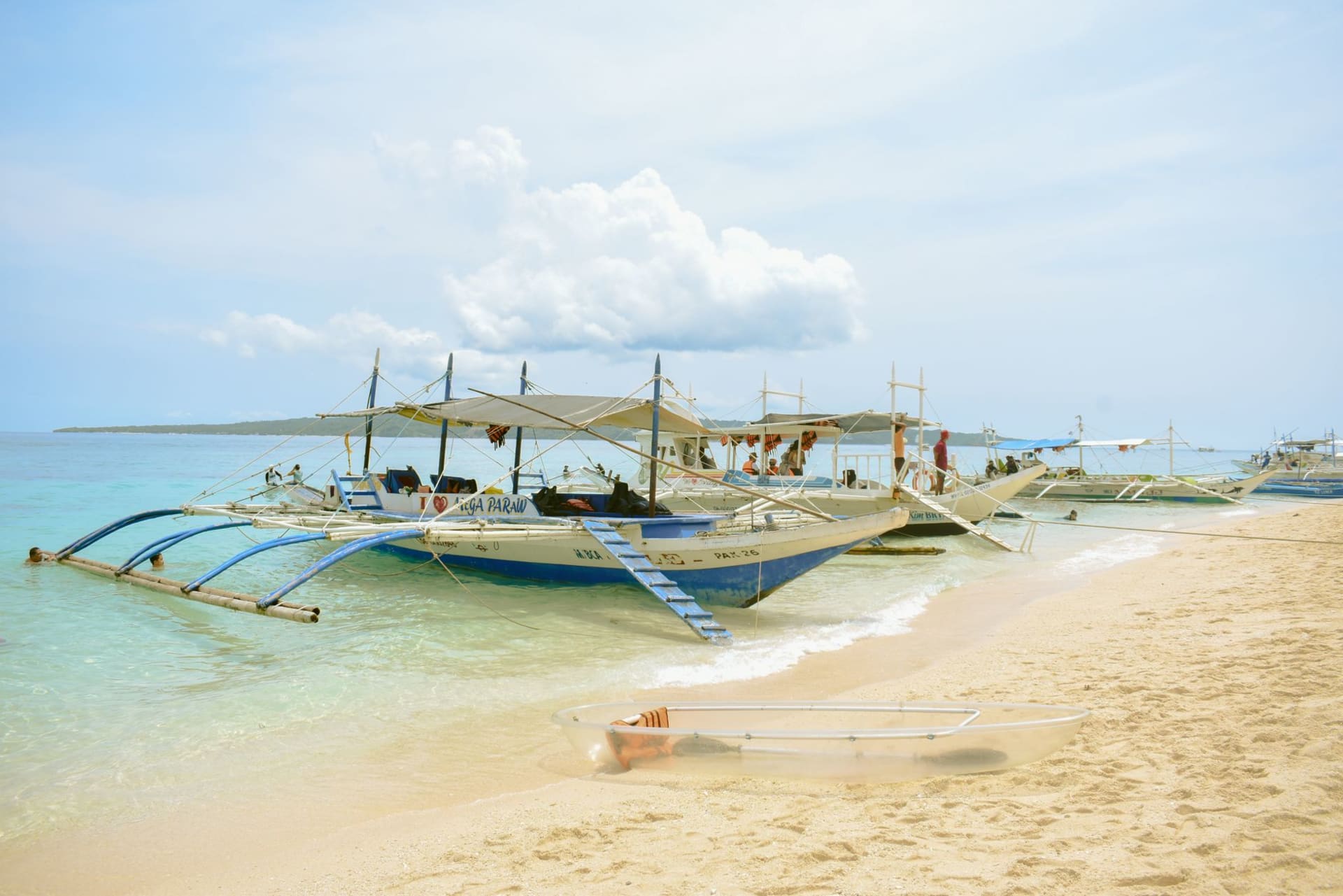 Alona Beach at low tide, the turquoise water retreating to reveal a band of white sand, outrigger bangka boats moored in the shallows at first light