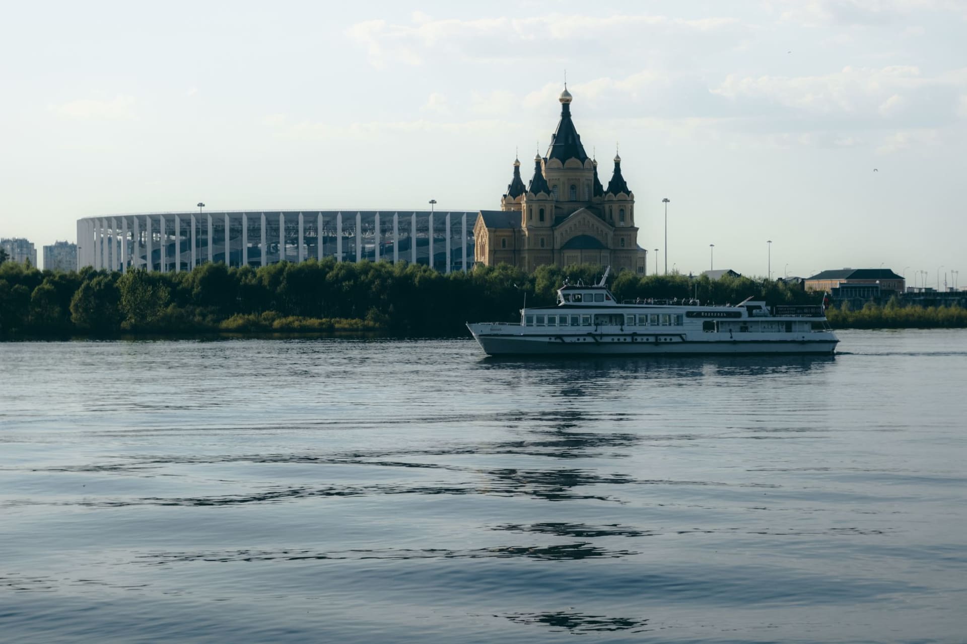 Ferry cruising on the Volga River with a cathedral and stadium on the Nizhny Novgorod embankment in the background