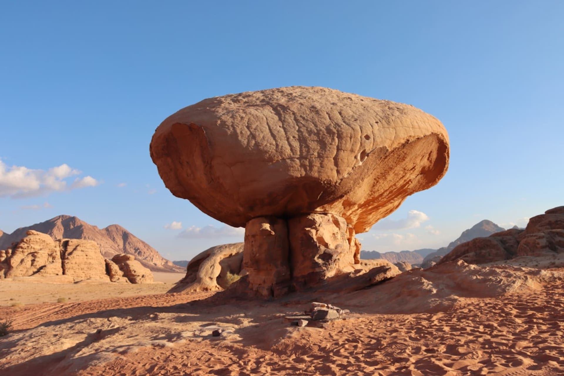 A wind-eroded sandstone mushroom formation standing isolated on the desert floor, its narrow stem and broad cap glowing orange against a clear blue desert sky