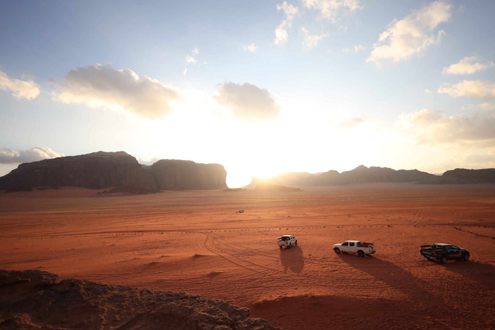 Sweeping red sand dunes glowing in late afternoon light against towering sandstone cliffs, a lone set of footprints tracking up the nearest dune face
