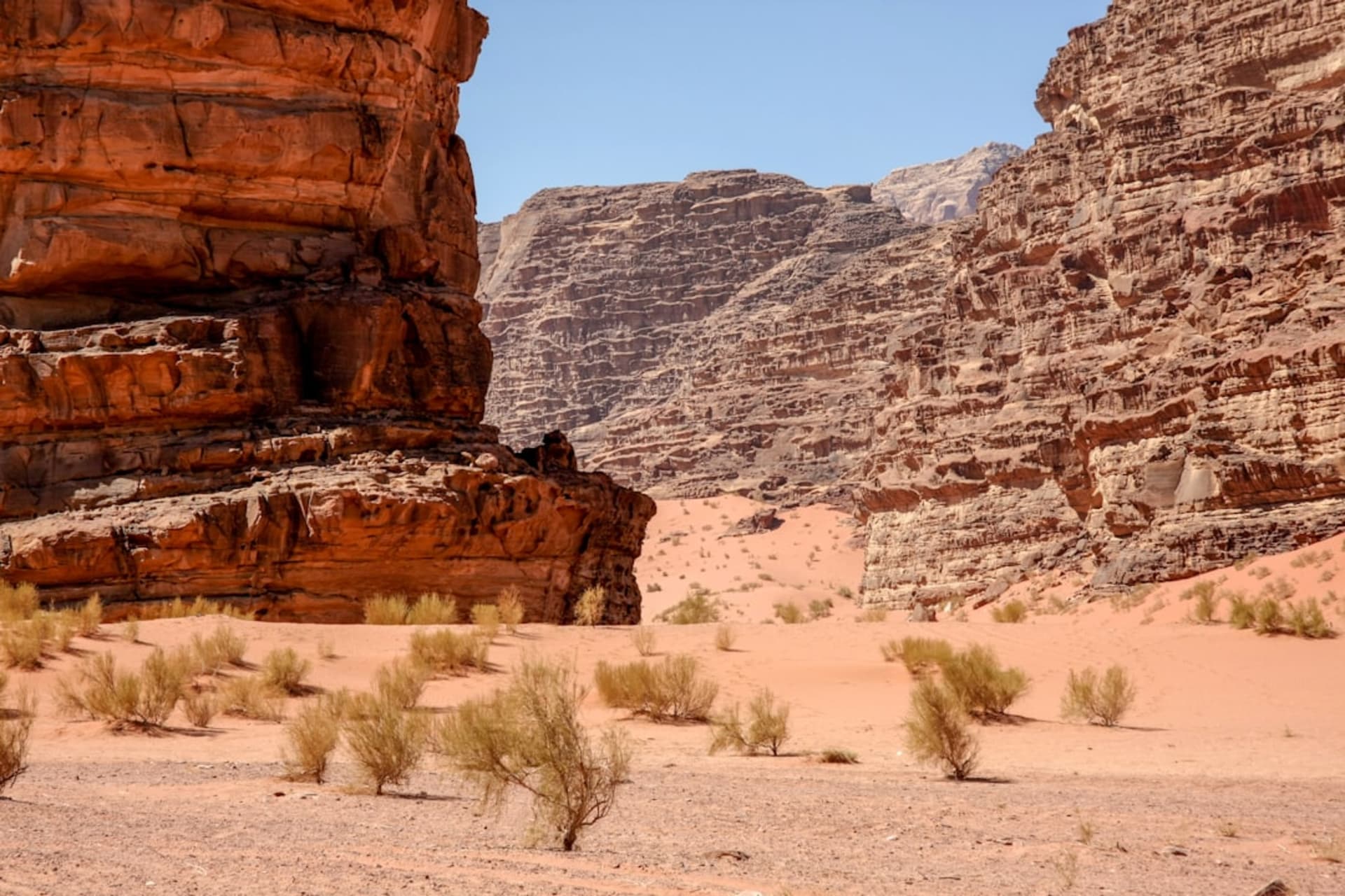 The Seven Pillars of Wisdom formation, a vast fractured sandstone massif glowing deep orange at sunset, the desert valley floor stretching out below its sheer face