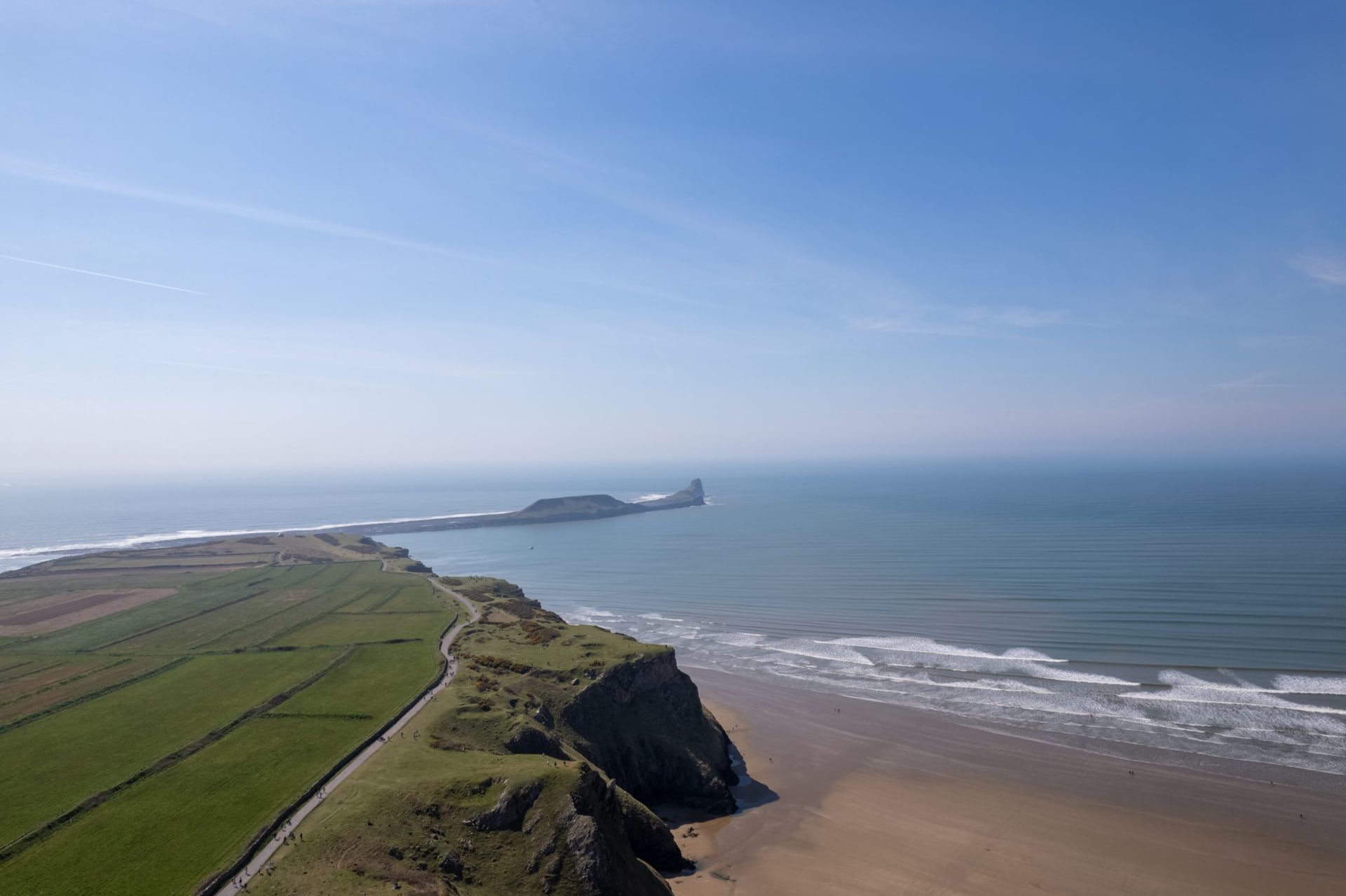 Rhossili Bay's three-mile sweep of sand at low tide, the tidal island of Worm's Head at the far end, golden afternoon light