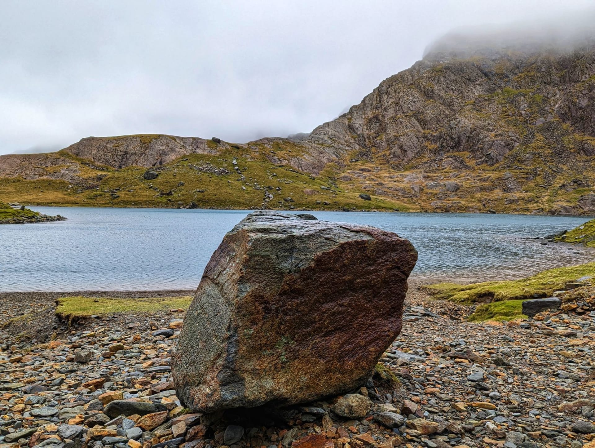 The summit ridge of Snowdon emerging from low cloud above the Llanberis Pass, lichen-grey boulders in the foreground