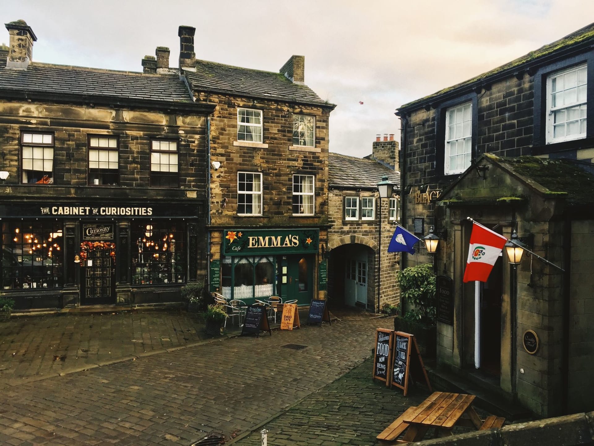 Haworth's steep cobblestone main street lined with dark millstone grit buildings climbing toward the church tower, empty in early morning light
