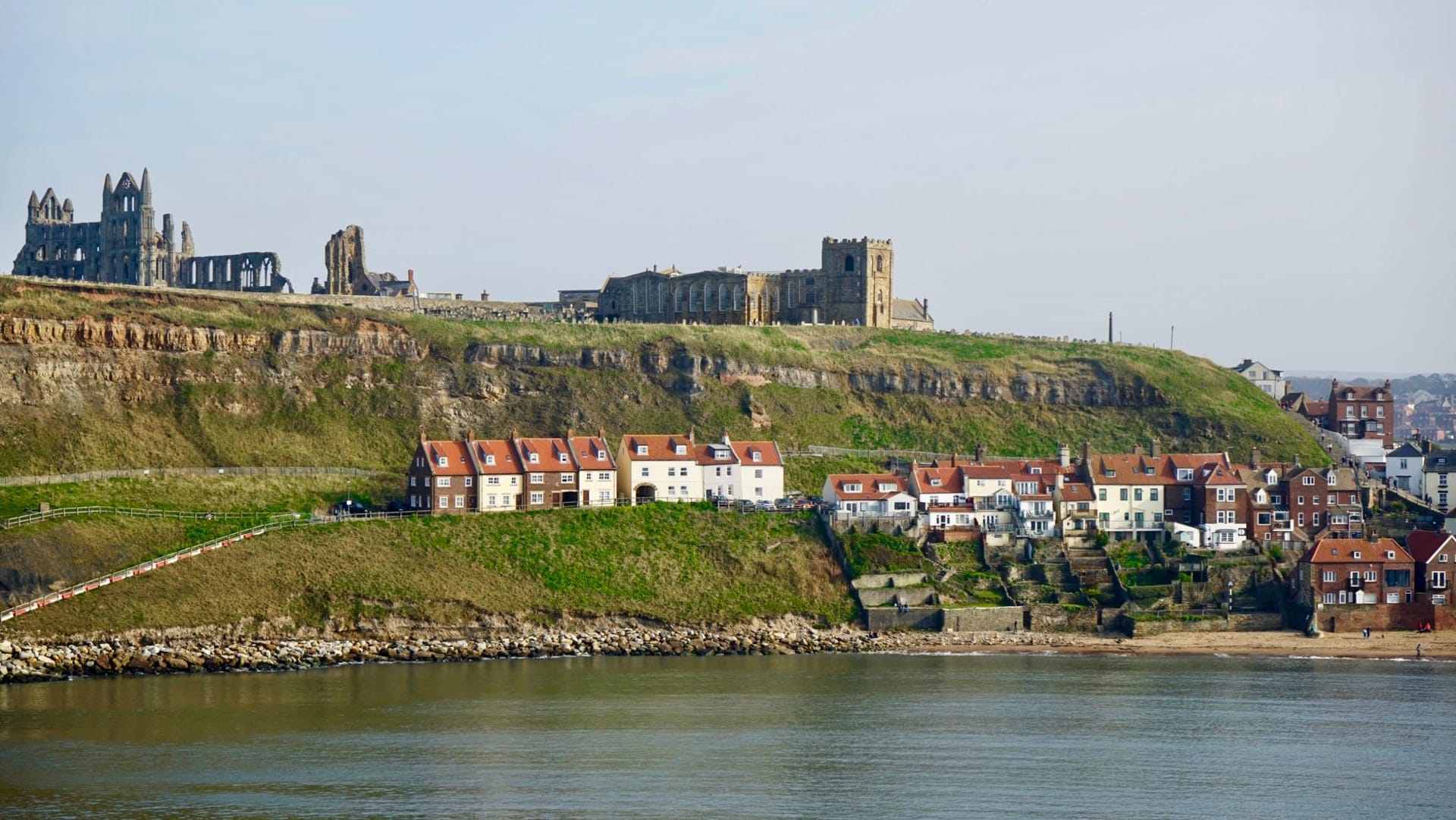 Robin Hood's Bay's tightly packed red-roofed cottages cascading down the cliff toward the rocky bay, a North Sea swell breaking white on the boulders below