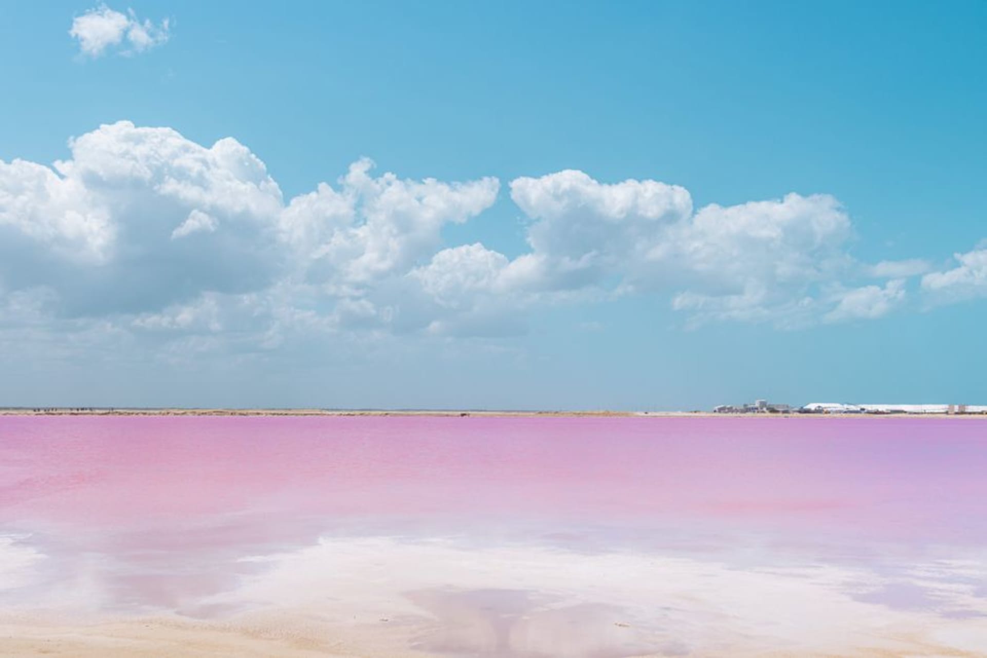 Bright pink saltwater lagoon with white salt mounds under a blue sky at Las Coloradas