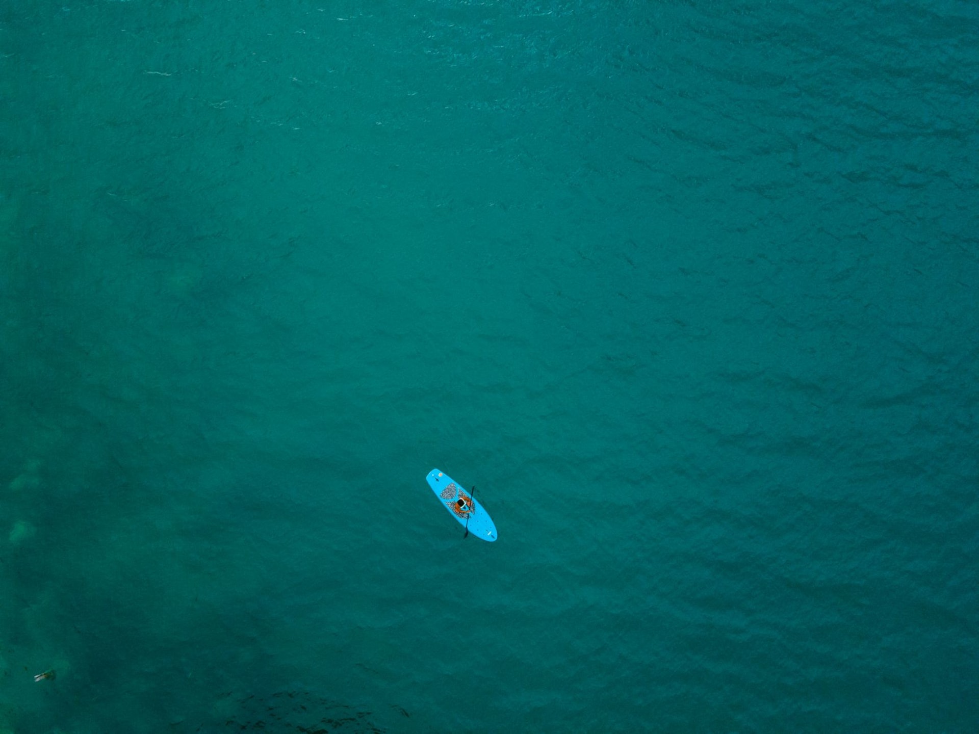 Bacalar's Laguna de los Siete Colores seen from a dock in early morning light, the lake shifting from pale turquoise to deep blue, a wooden sailboat anchored in the shallows