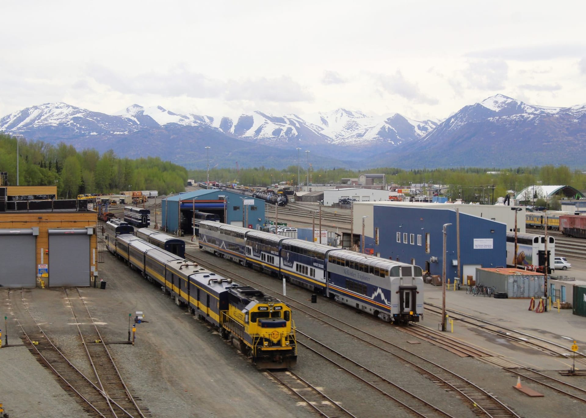 Las cimas nevadas de la cordillera Kluane elevándose dramáticamente sobre el borde arbolado de Haines Junction, con una solitaria carretera cortando el primer plano