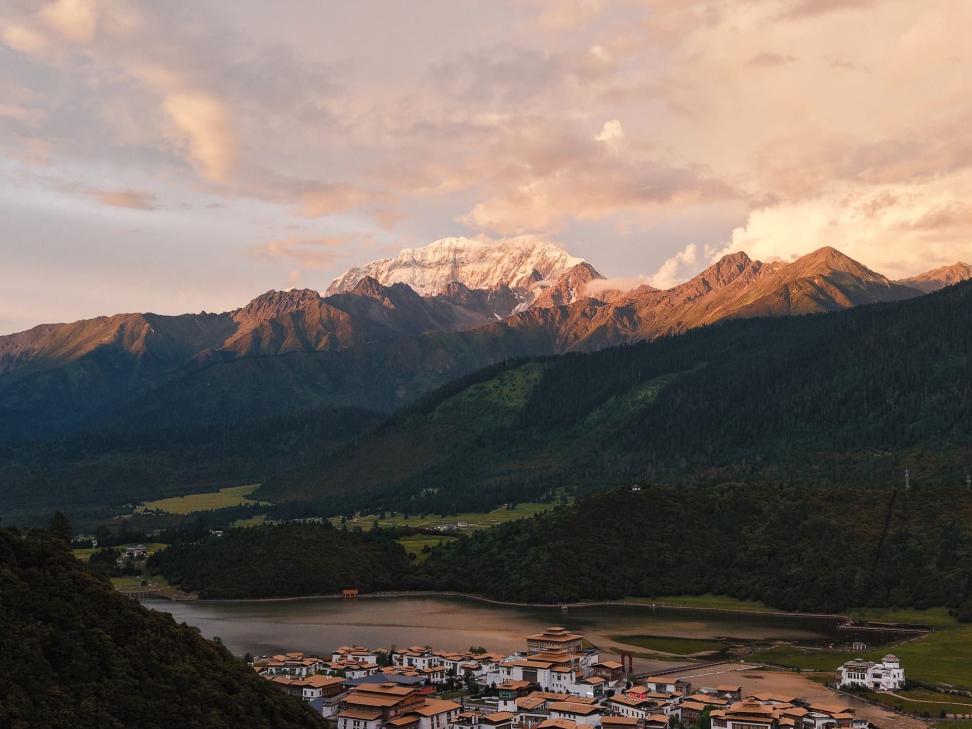 Ganden Sumtseling Monastery at golden hour, white-washed walls rising above a valley of barley fields