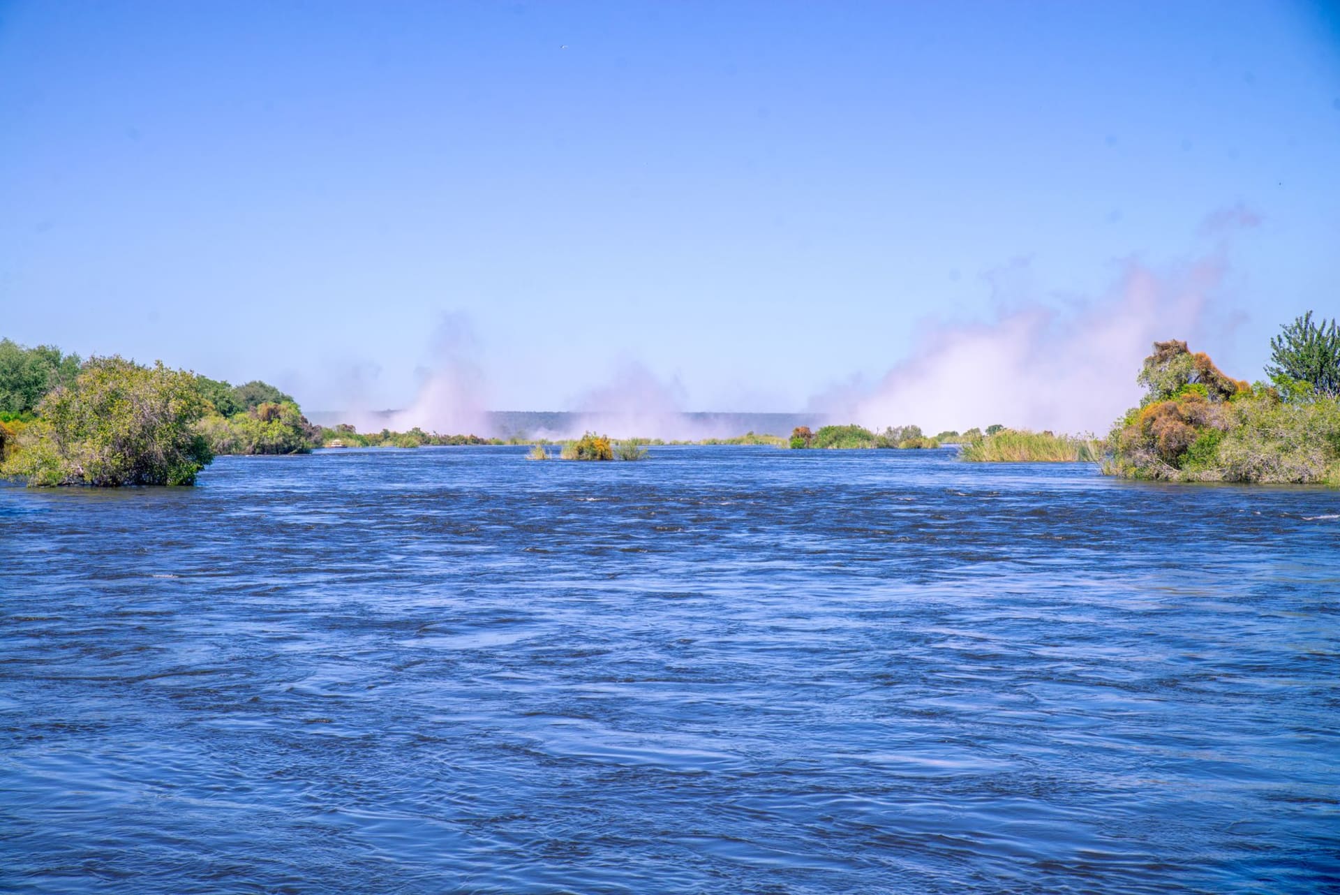 A wooden canoe drifting past a group of elephants wading in the Lower Zambezi River, the Zimbabwean escarpment visible in golden morning light