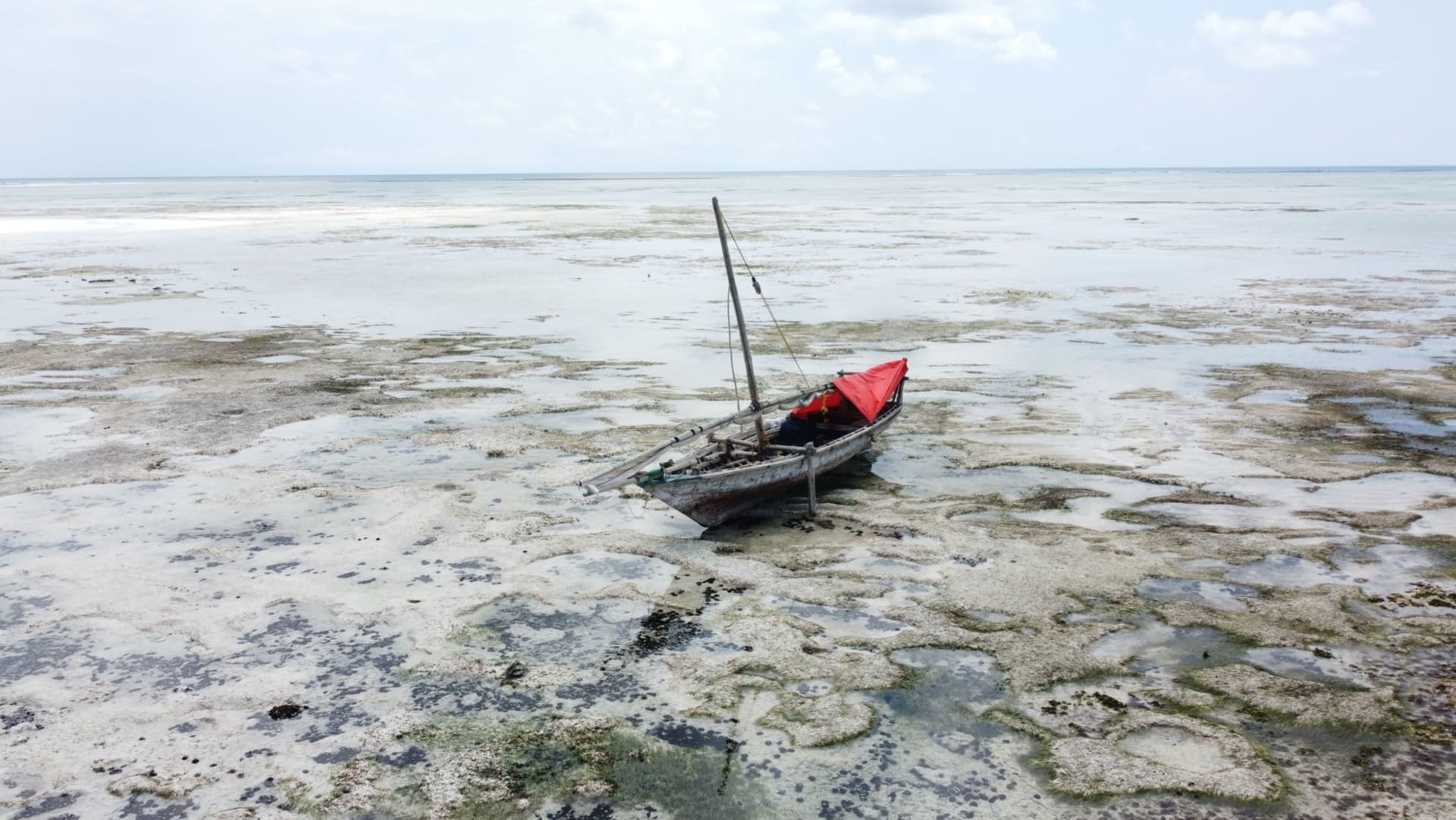 A lone dhow anchored over a shallow turquoise reef at Matemwe, with a palm-fringed beach in the background