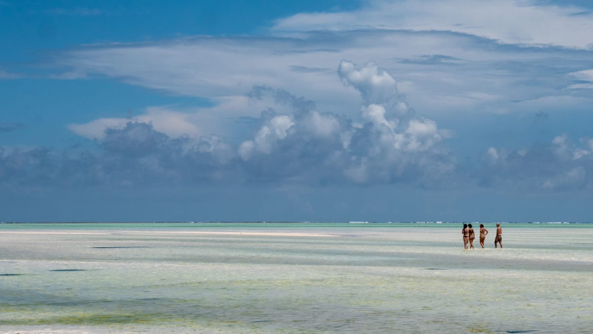 A kitesurfer launching over shallow turquoise water at Paje beach with a white sand flat stretching to the horizon