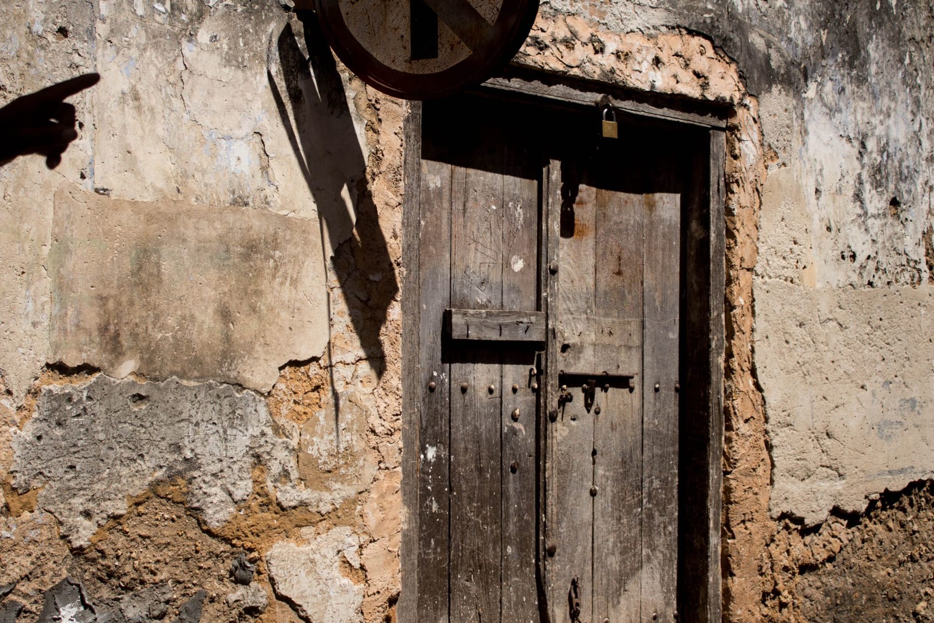 An ornately carved wooden door in a coral-stone archway on a narrow Stone Town alley at golden hour
