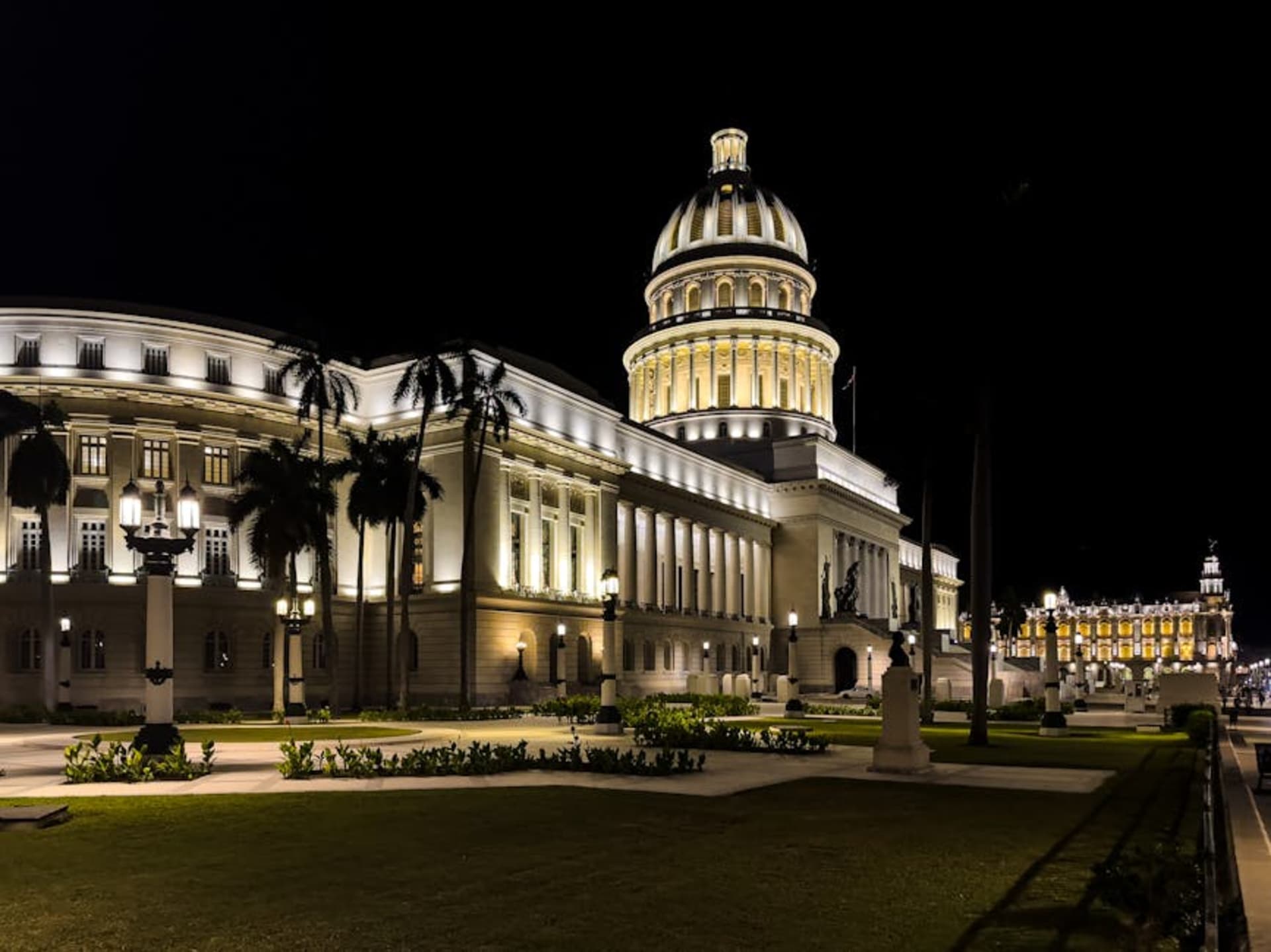 Havana street at night with warm light spilling from doorways and vintage cars