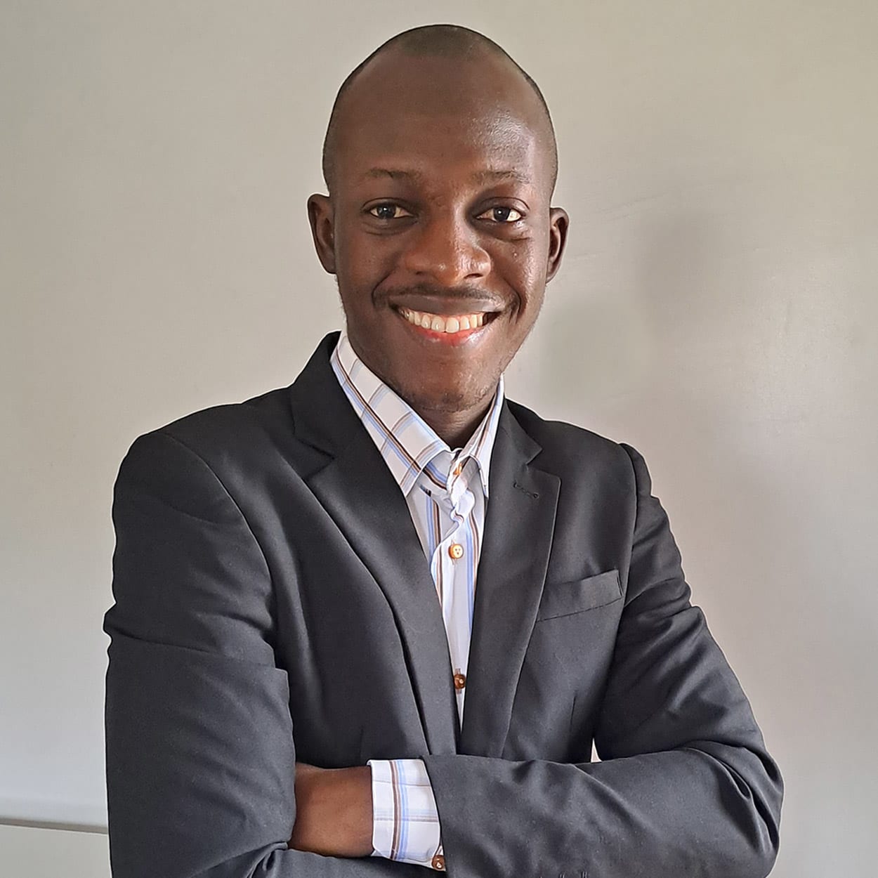 Isaac Oluwayinka, smiling with arms folded, in a dark blazer and a striped shirt