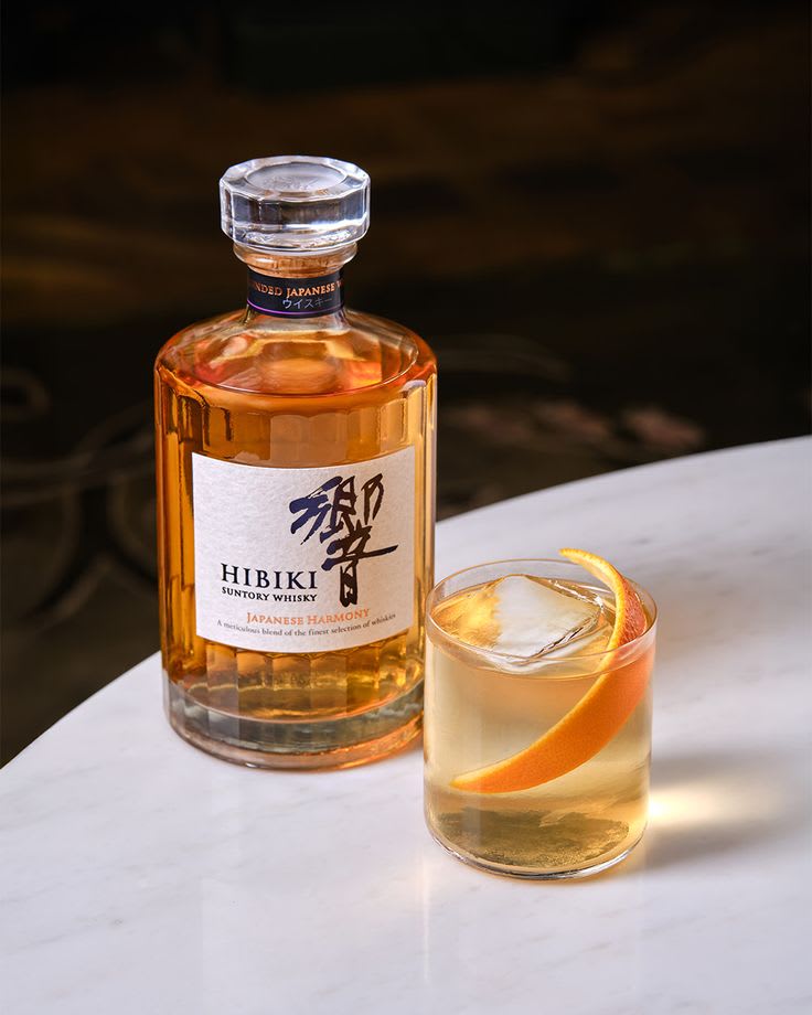 Japanese whisky bottle beside a highball glass with ice and citrus garnish on a light marble surface