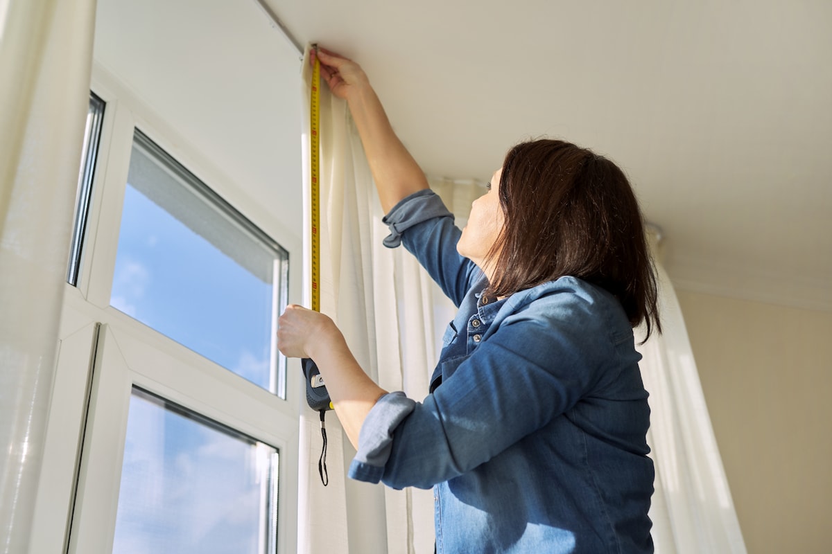 Woman on ladder measuring a hanging curtain