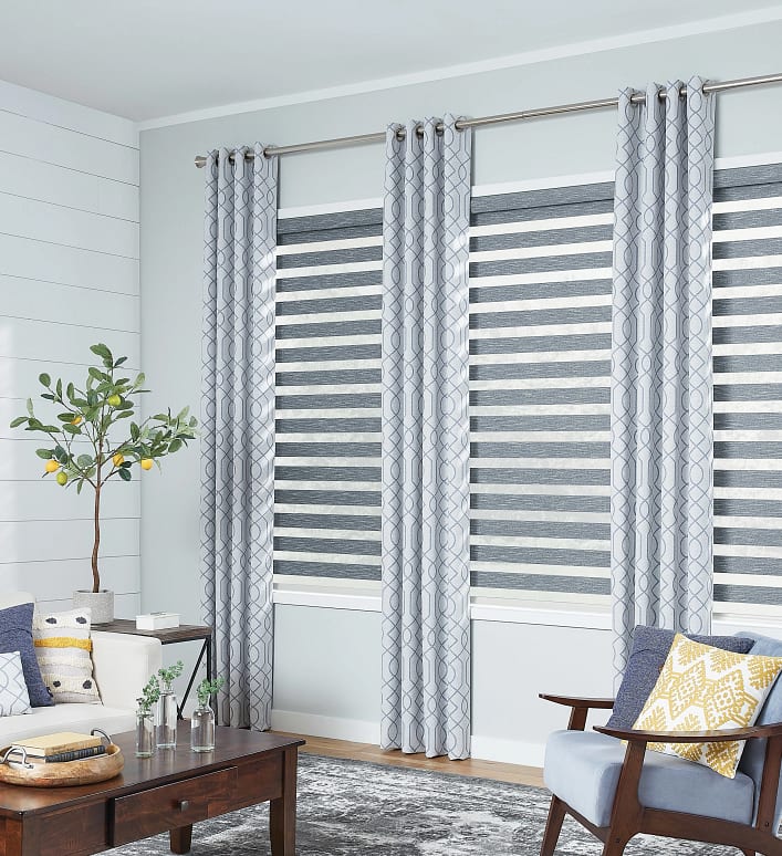 Layered window shades in a modern living room with tall windows, showcasing custom window treatment options
