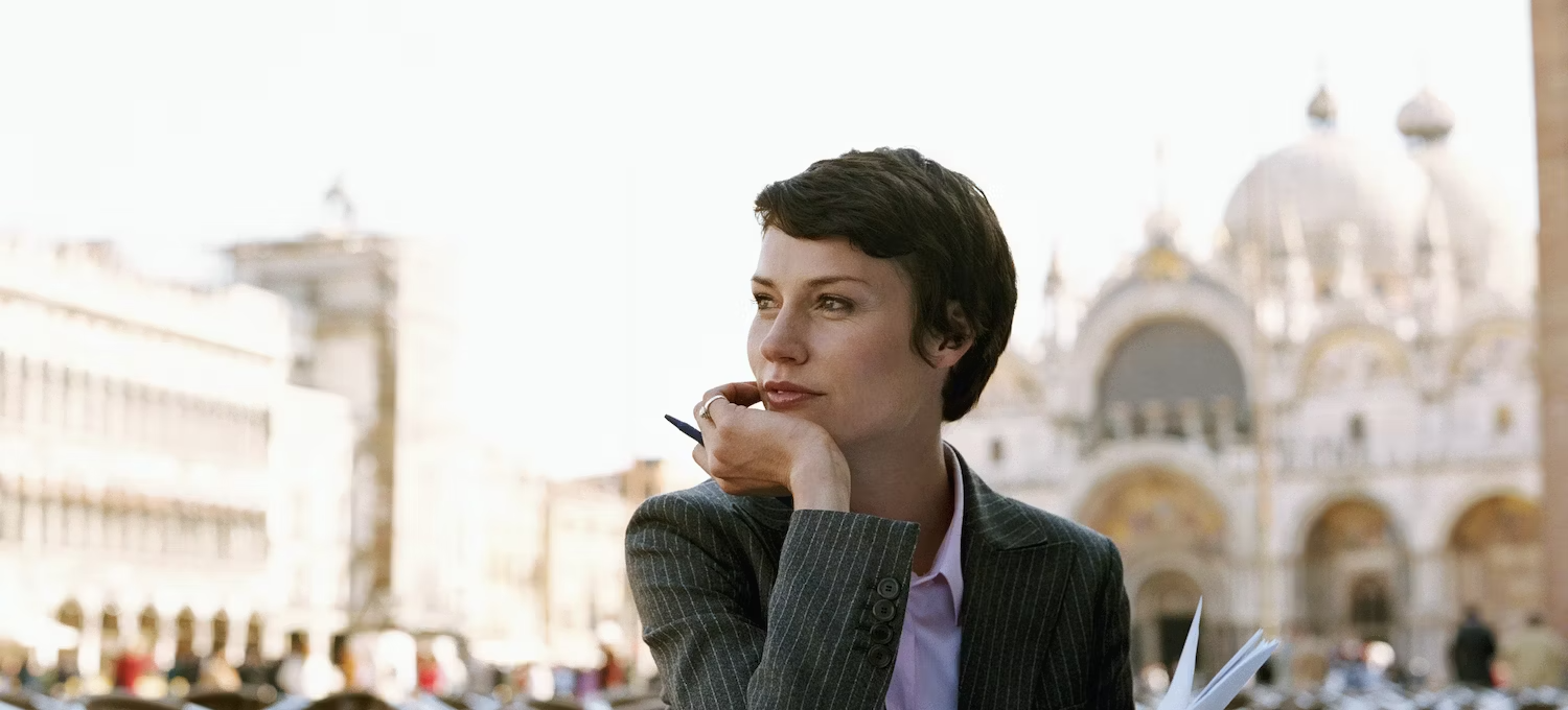 [Featured Image] A businesswoman in a blazer sits outside at a cafe and considers a career in hospitality management.