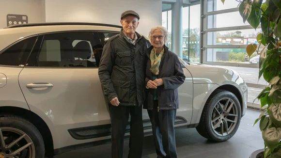 Le couple nonagénaire, souriant et élégant, savoure le confort et le prestige de l'habitacle de leur Porsche Macan.